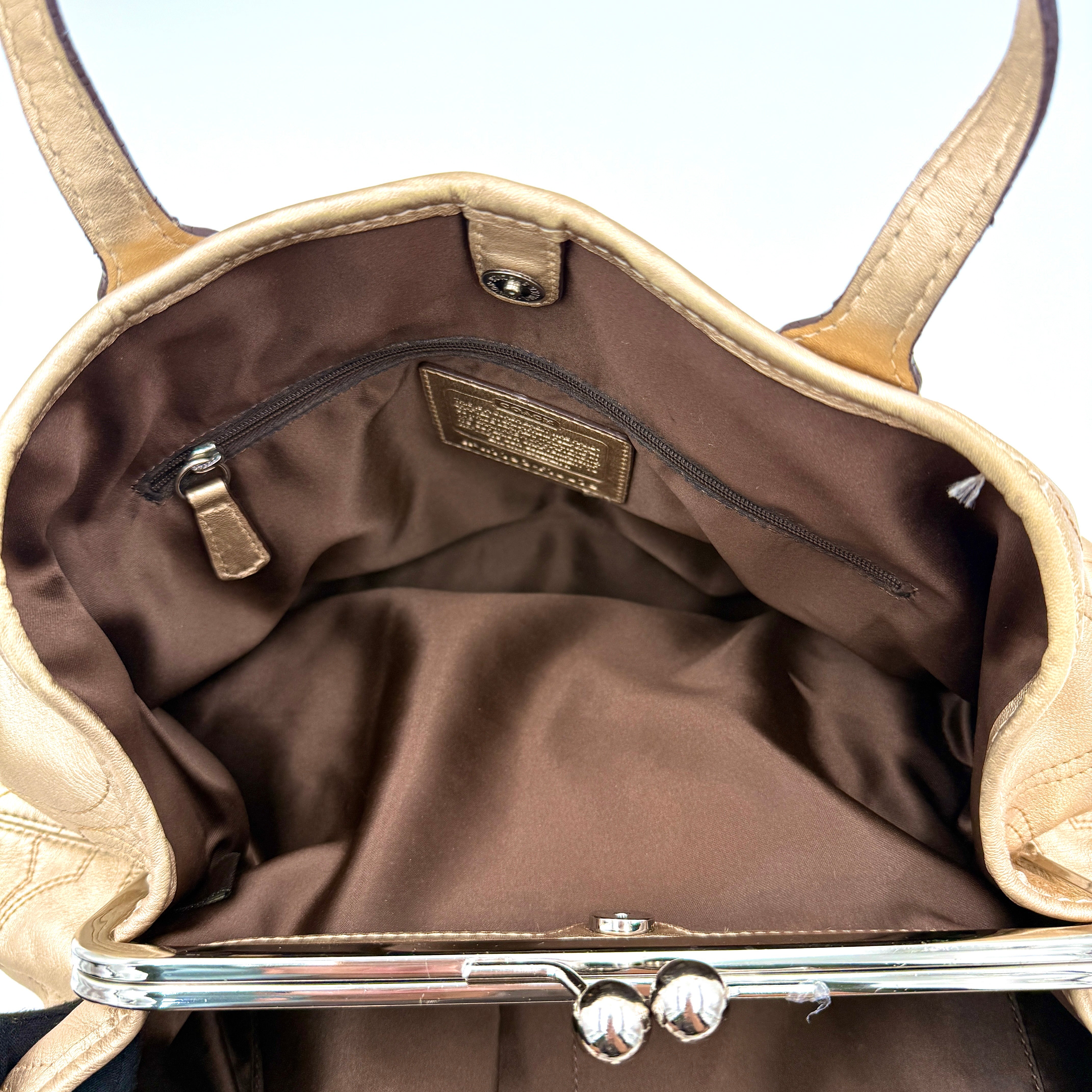 Coach metallic gold shoulder bag with signature embossed leather, double top handles, and a kisslock closure set against a clean background.