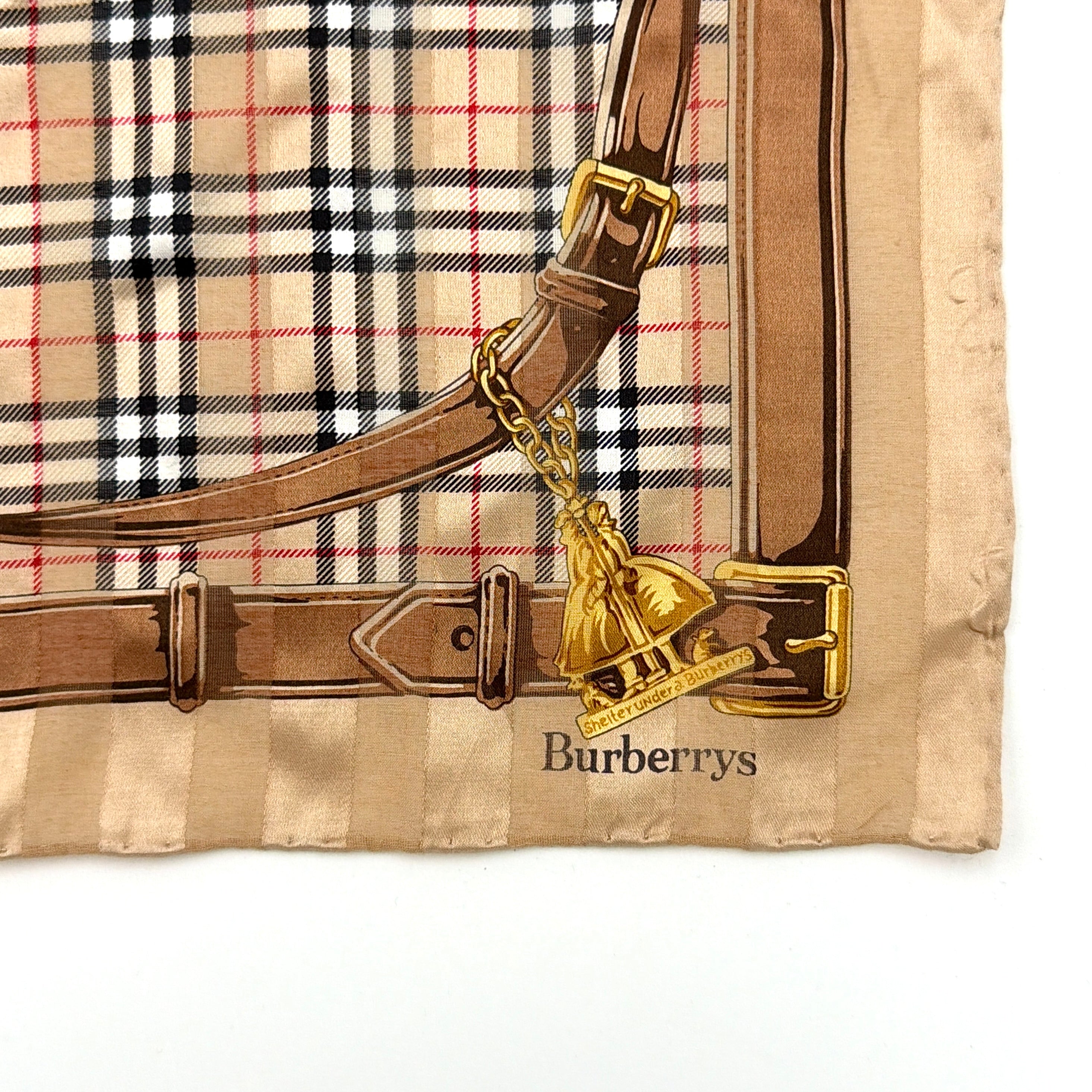 Editorial image of a Burberry silk bandana featuring Nova Check and equestrian-inspired harness motif in beige and gold tones.