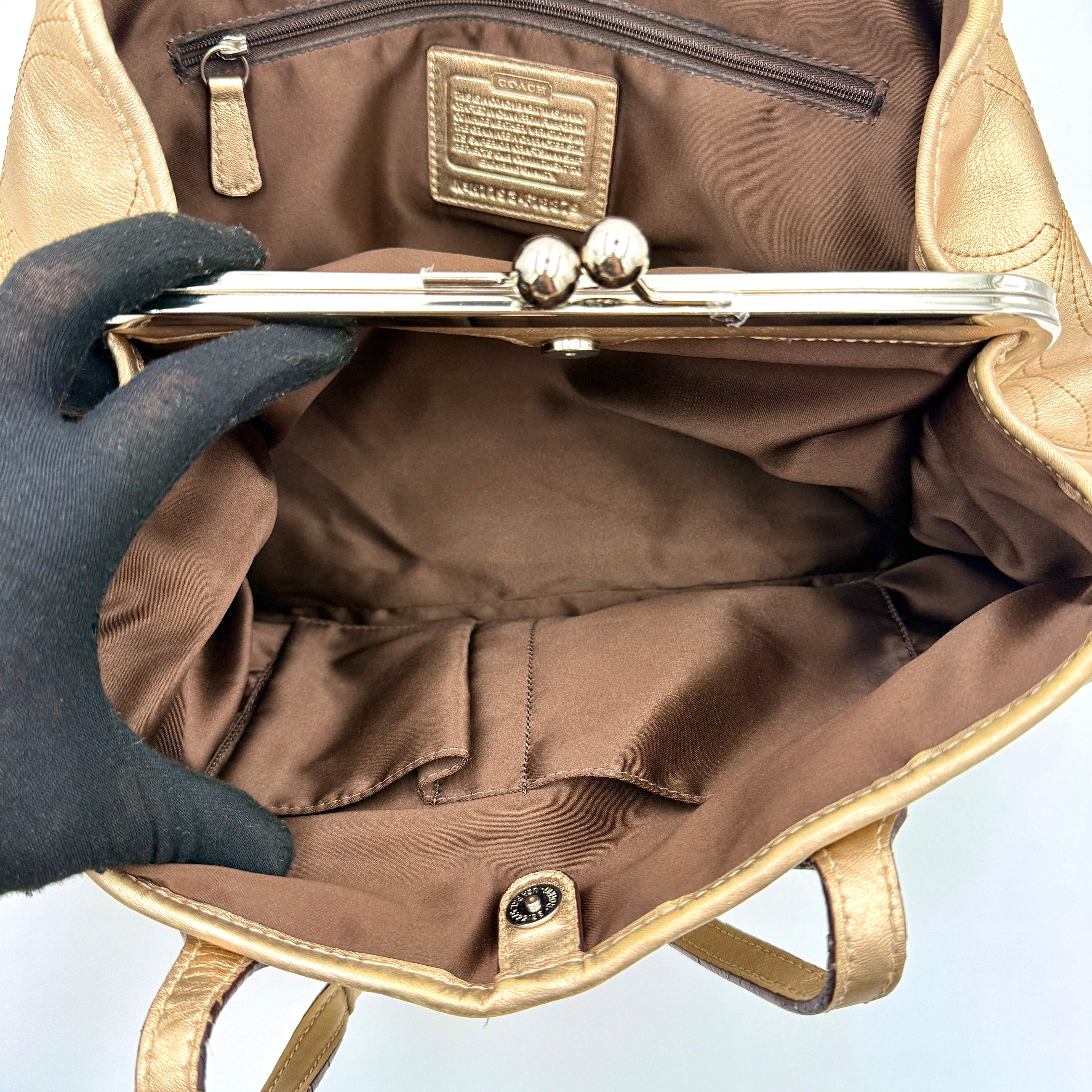 Coach metallic gold shoulder bag with signature embossed leather, double top handles, and a kisslock closure set against a clean background.