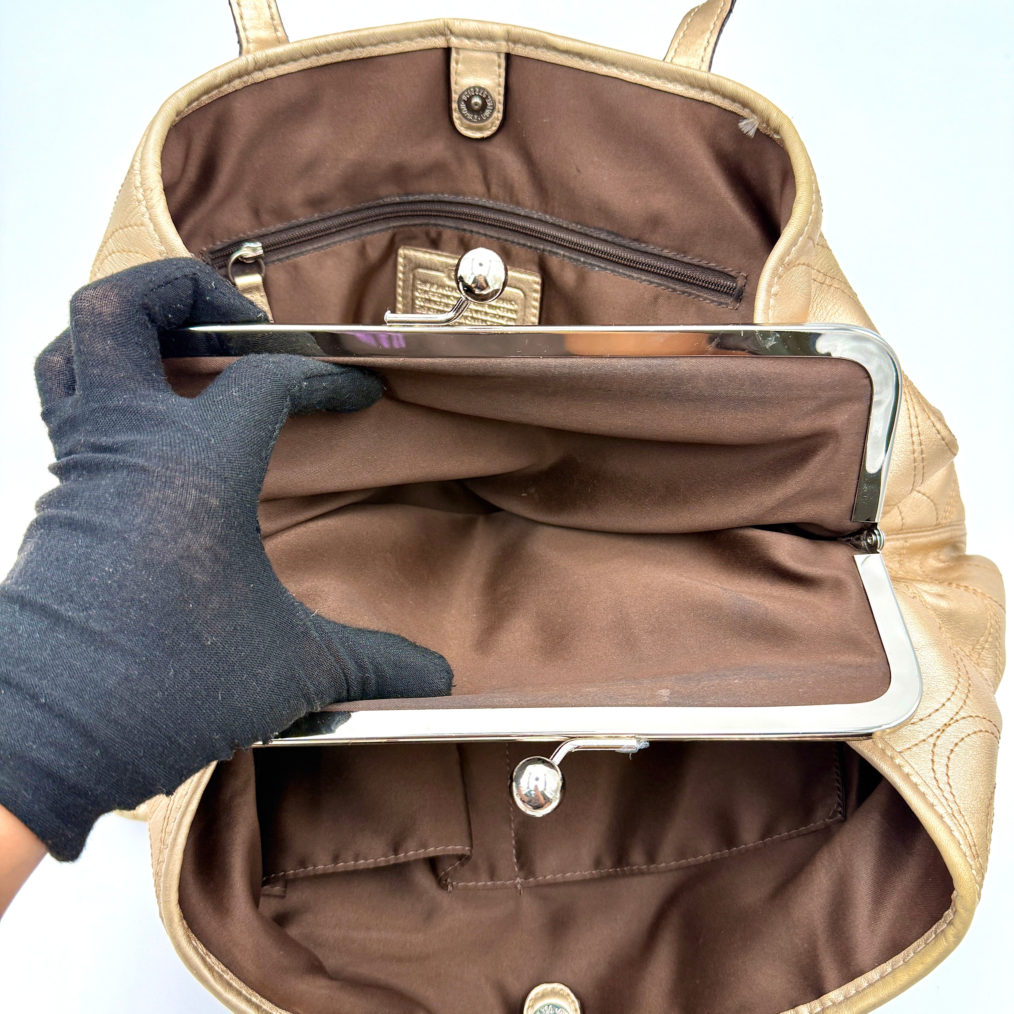 Coach metallic gold shoulder bag with signature embossed leather, double top handles, and a kisslock closure set against a clean background.
