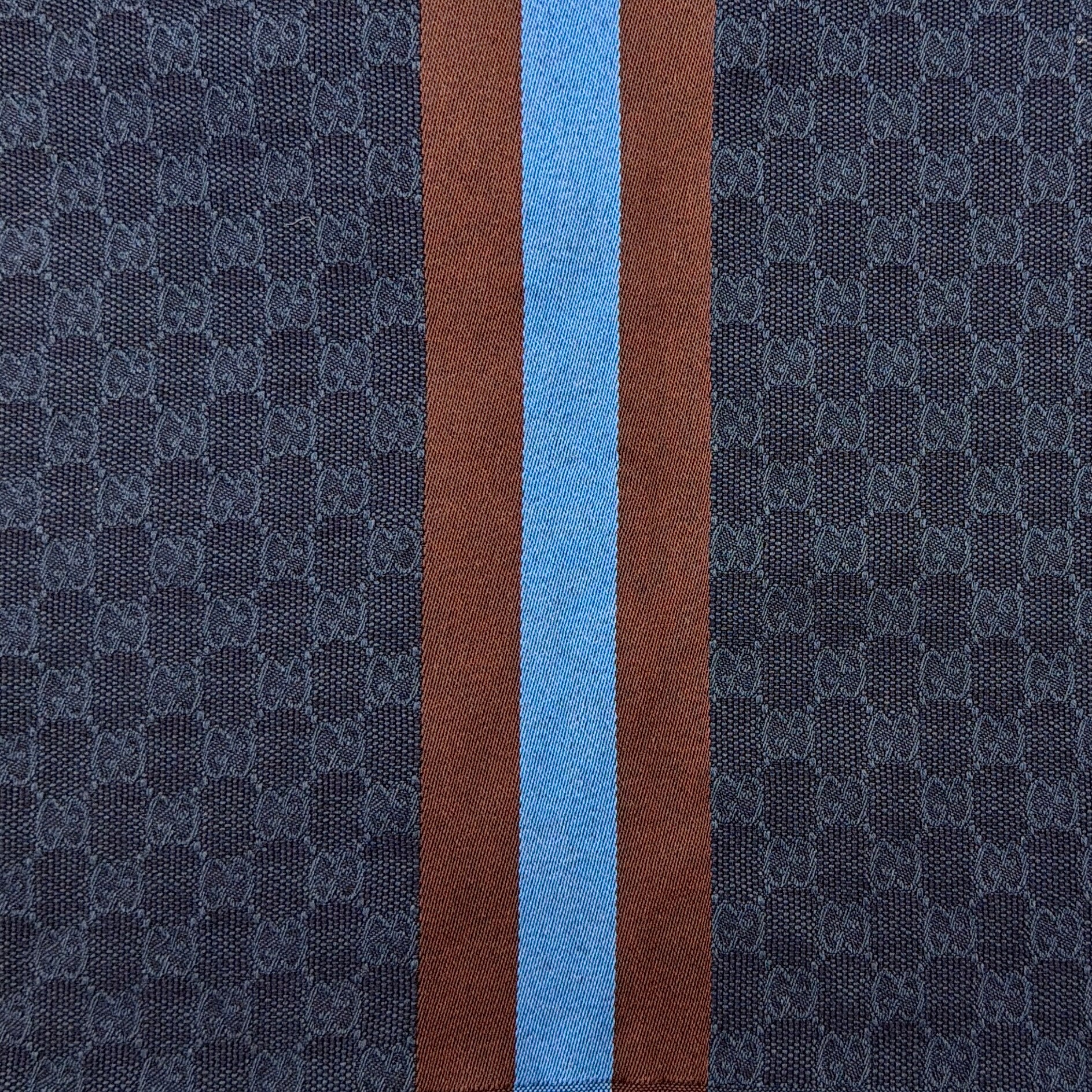 Gucci GG Monogram navy blue scarf with brown and blue Sherry Web stripes and fringed edges, artfully arranged to showcase its luxurious texture.