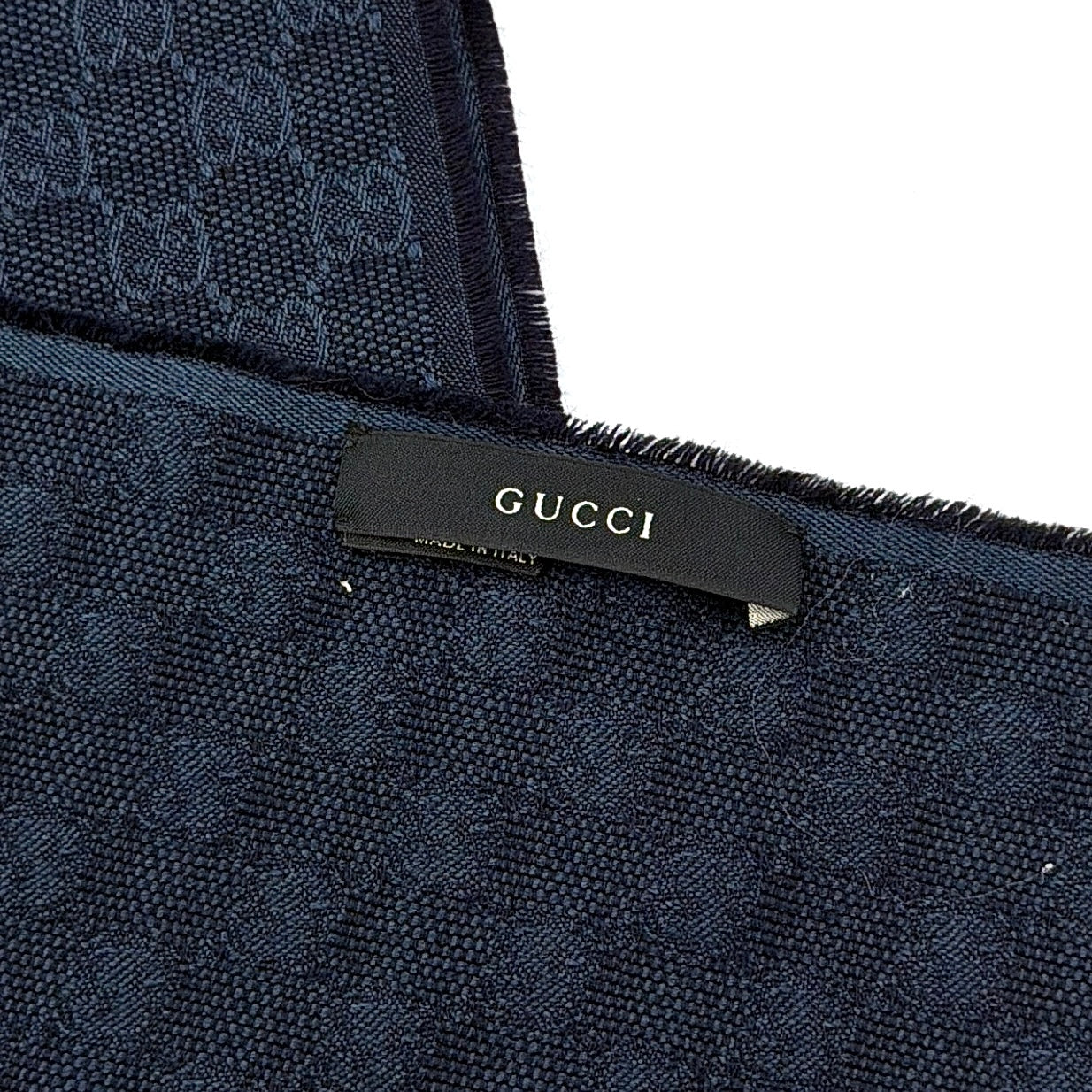 Gucci GG Monogram navy blue scarf with brown and blue Sherry Web stripes and fringed edges, artfully arranged to showcase its luxurious texture.