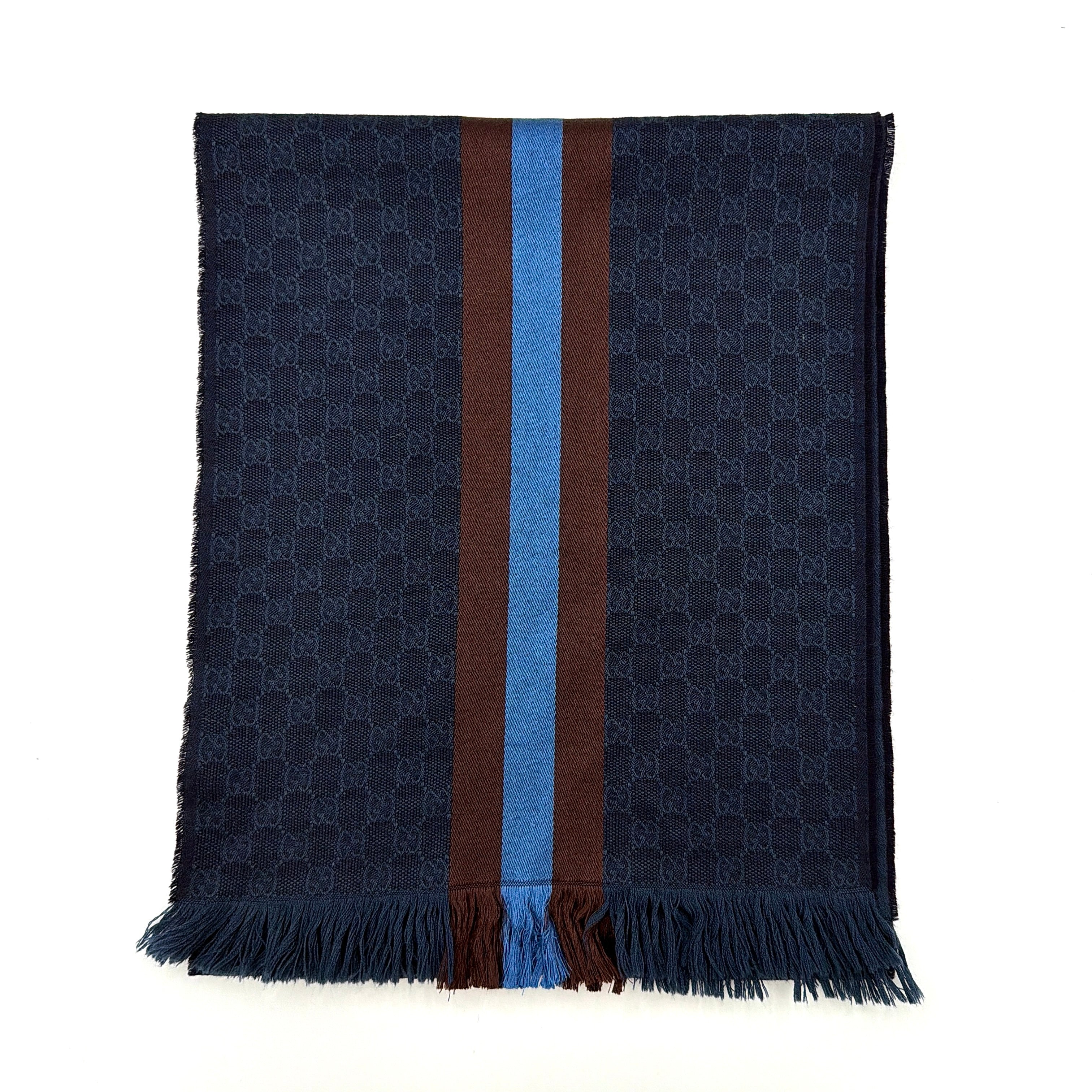 Gucci GG Monogram navy blue scarf with brown and blue Sherry Web stripes and fringed edges, artfully arranged to showcase its luxurious texture.