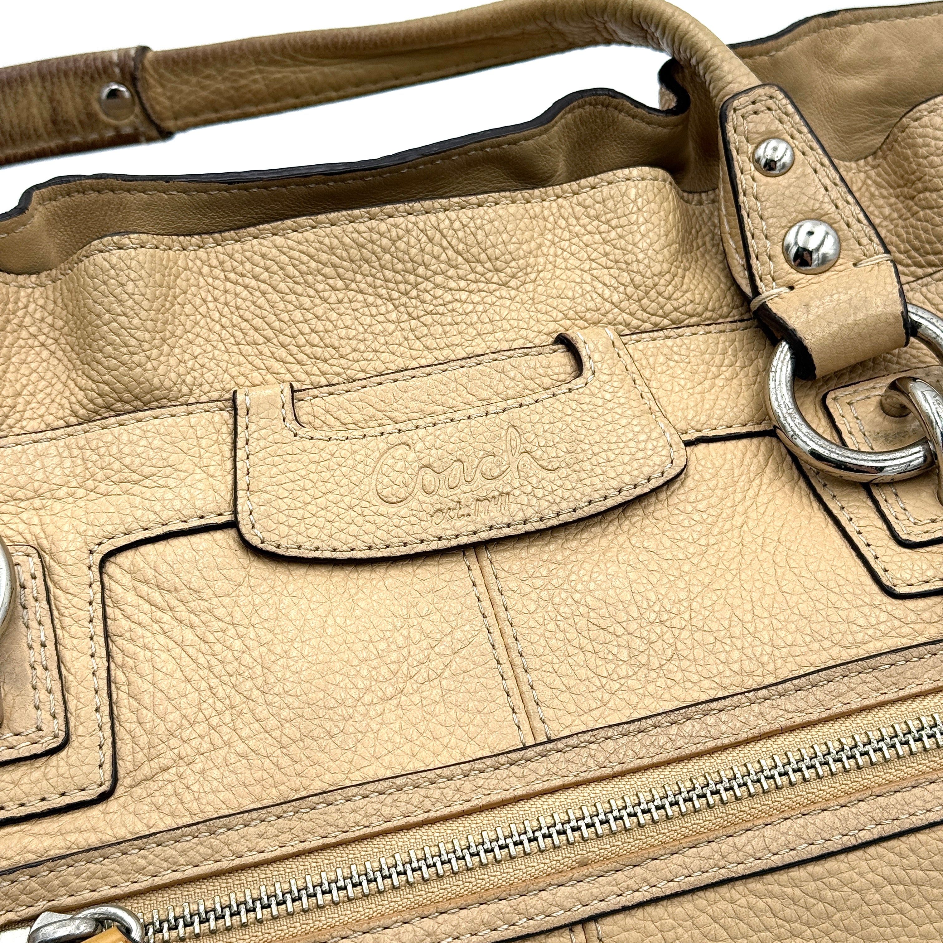 Coach Penelope handbag in cream pebble leather with rolled handles and silver-tone hardware against a white background.