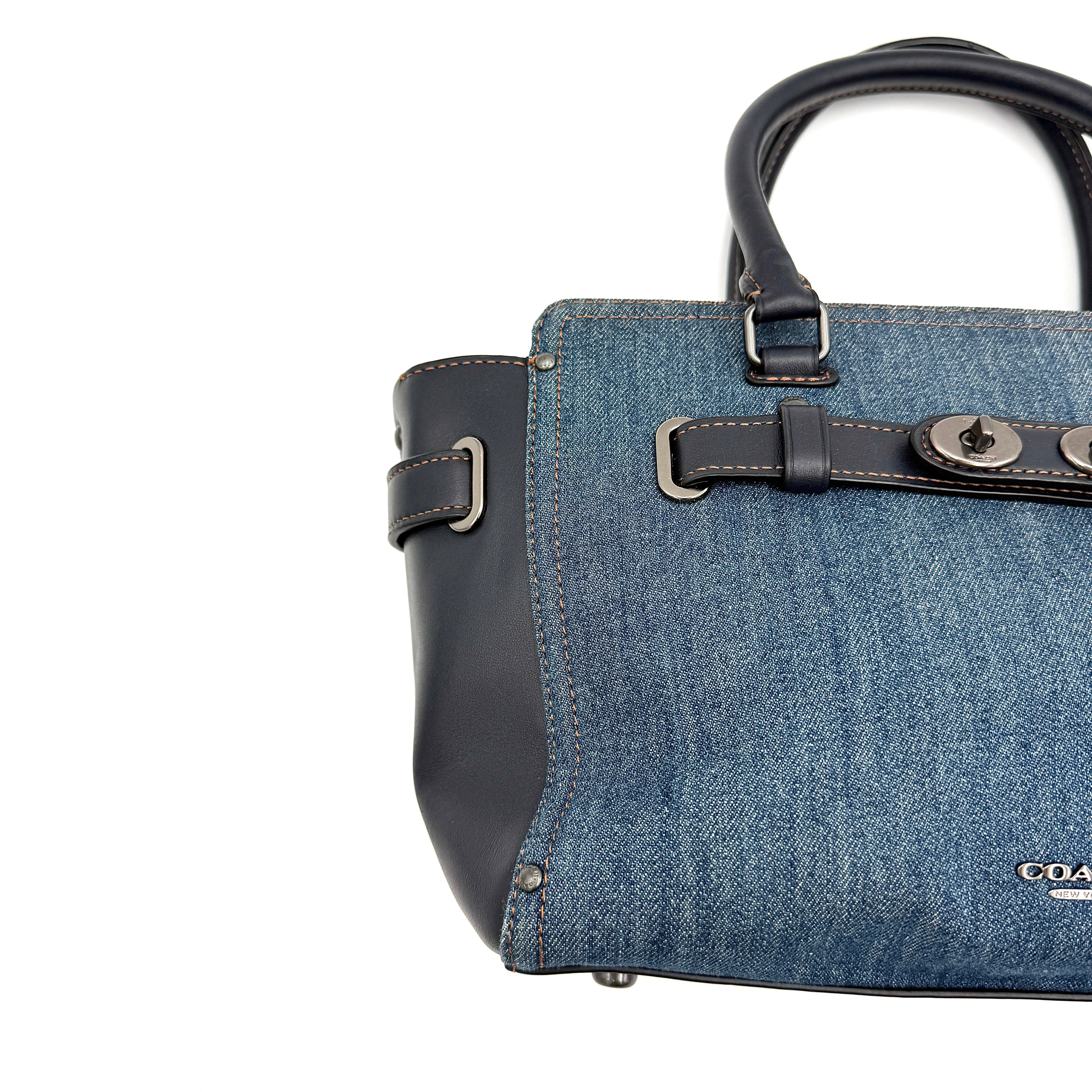 Coach Swagger 27 handbag in blue denim with navy leather trim and detachable strap, featuring prominent double turn-lock hardware and floral interior.