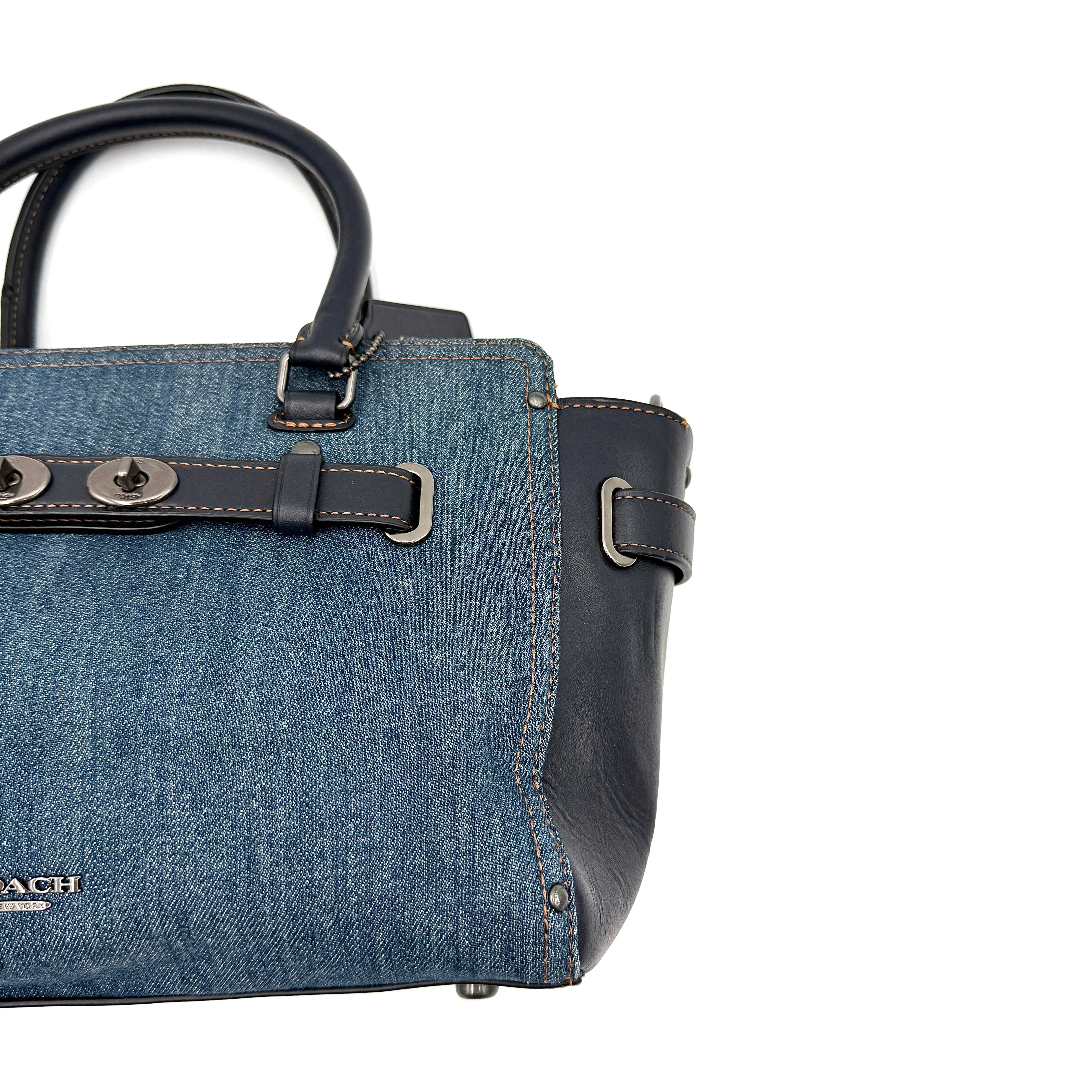 Coach Swagger 27 handbag in blue denim with navy leather trim and detachable strap, featuring prominent double turn-lock hardware and floral interior.