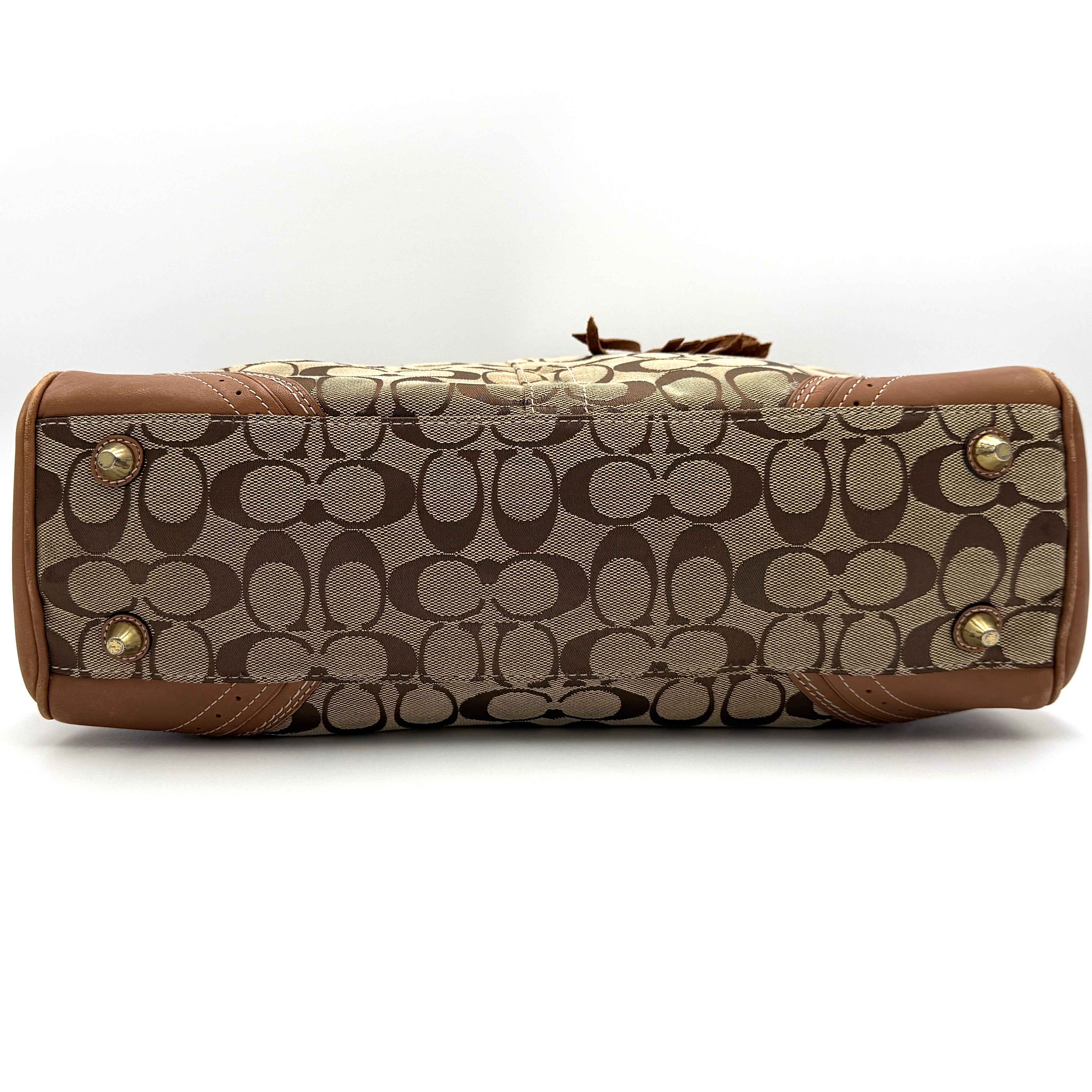Coach Signature Hampton Carryall Shoulder Bag in beige and tan canvas with caramel leather trim, gold hardware, and tassel detail, shown standing upright.