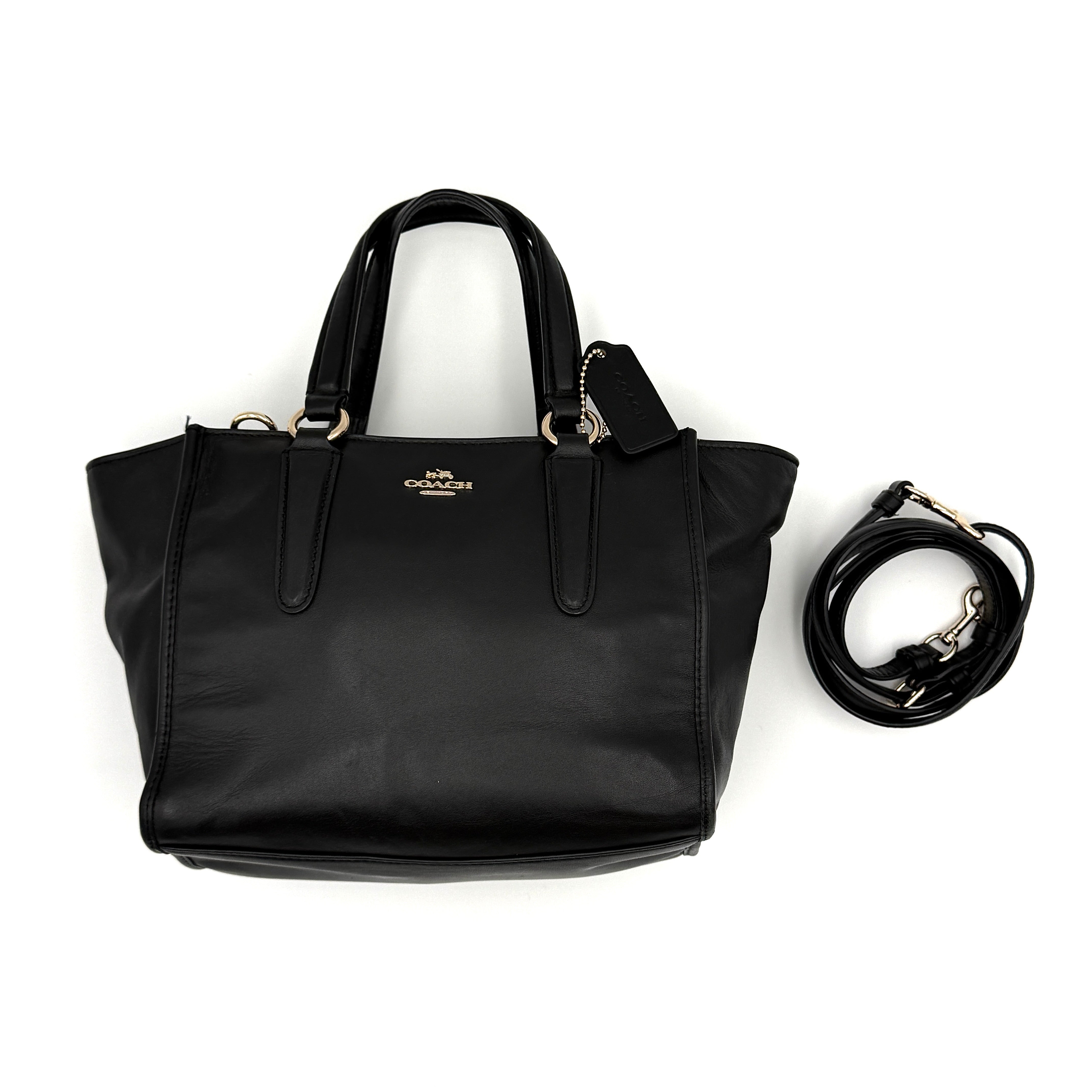 The Coach 2Way Mini Crosby Carryall Handbag in smooth black leather with gold-tone hardware, top handles, and detachable strap displayed alongside.