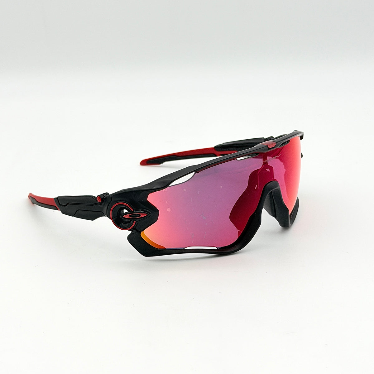 Oakley Jawbreaker Prizm sunglasses in matte black and red with pink-red Prizm lenses, shown with a black Oakley hard case and extra nose pad.