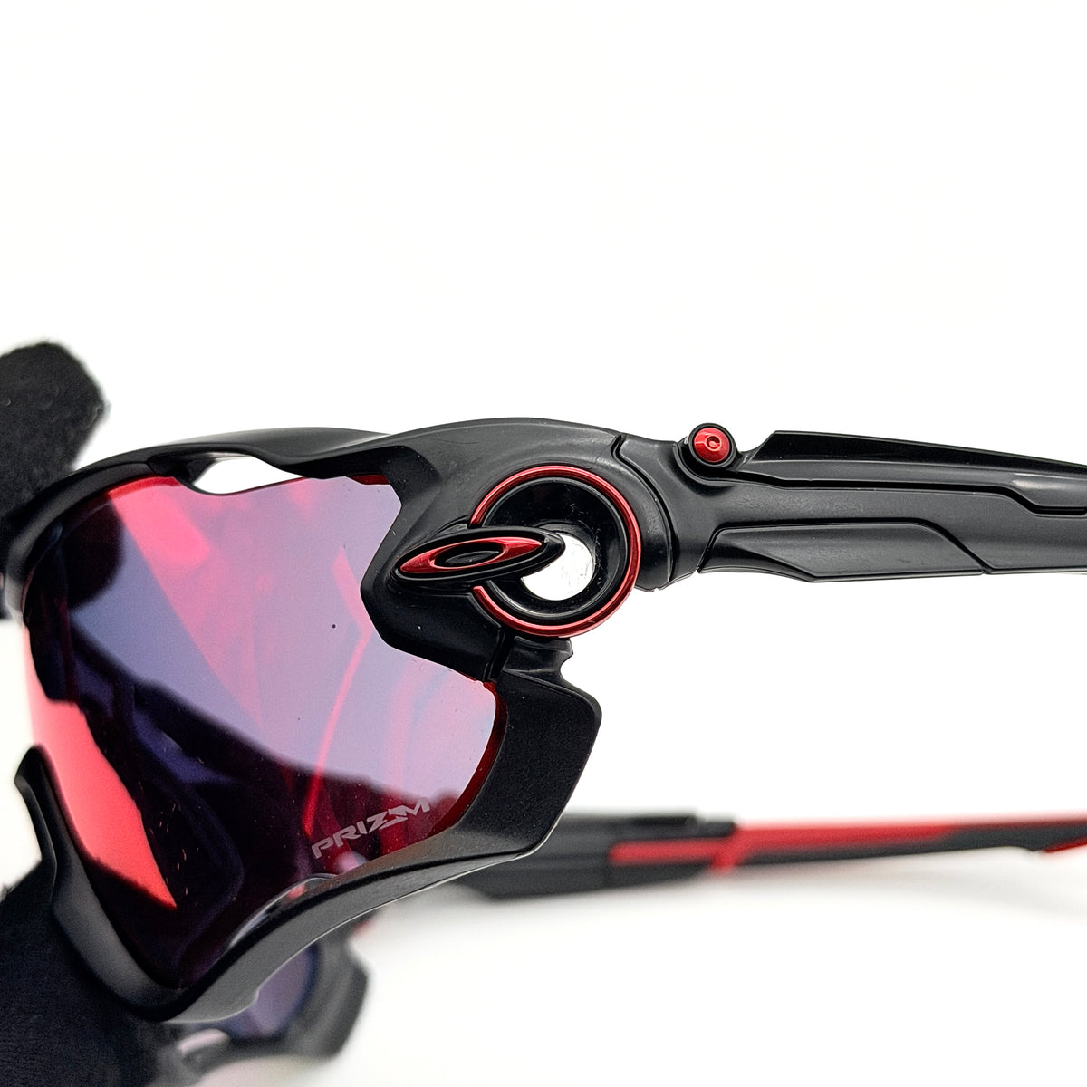 Oakley Jawbreaker Prizm sunglasses in matte black and red with pink-red Prizm lenses, shown with a black Oakley hard case and extra nose pad.