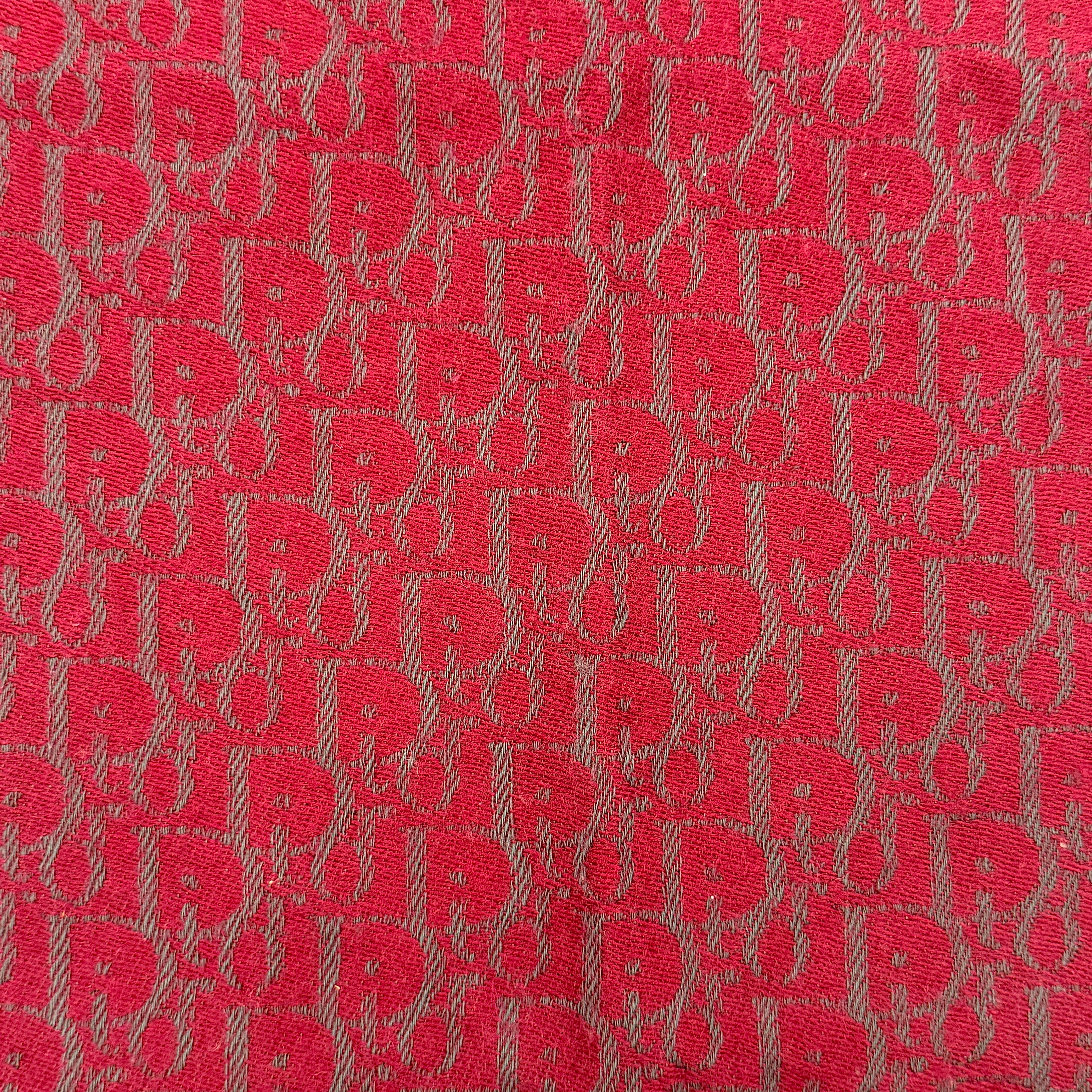 A red Dior Oblique Trotter wool scarf with all-over monogram pattern, navy border, stripe detail, and fringe trim.