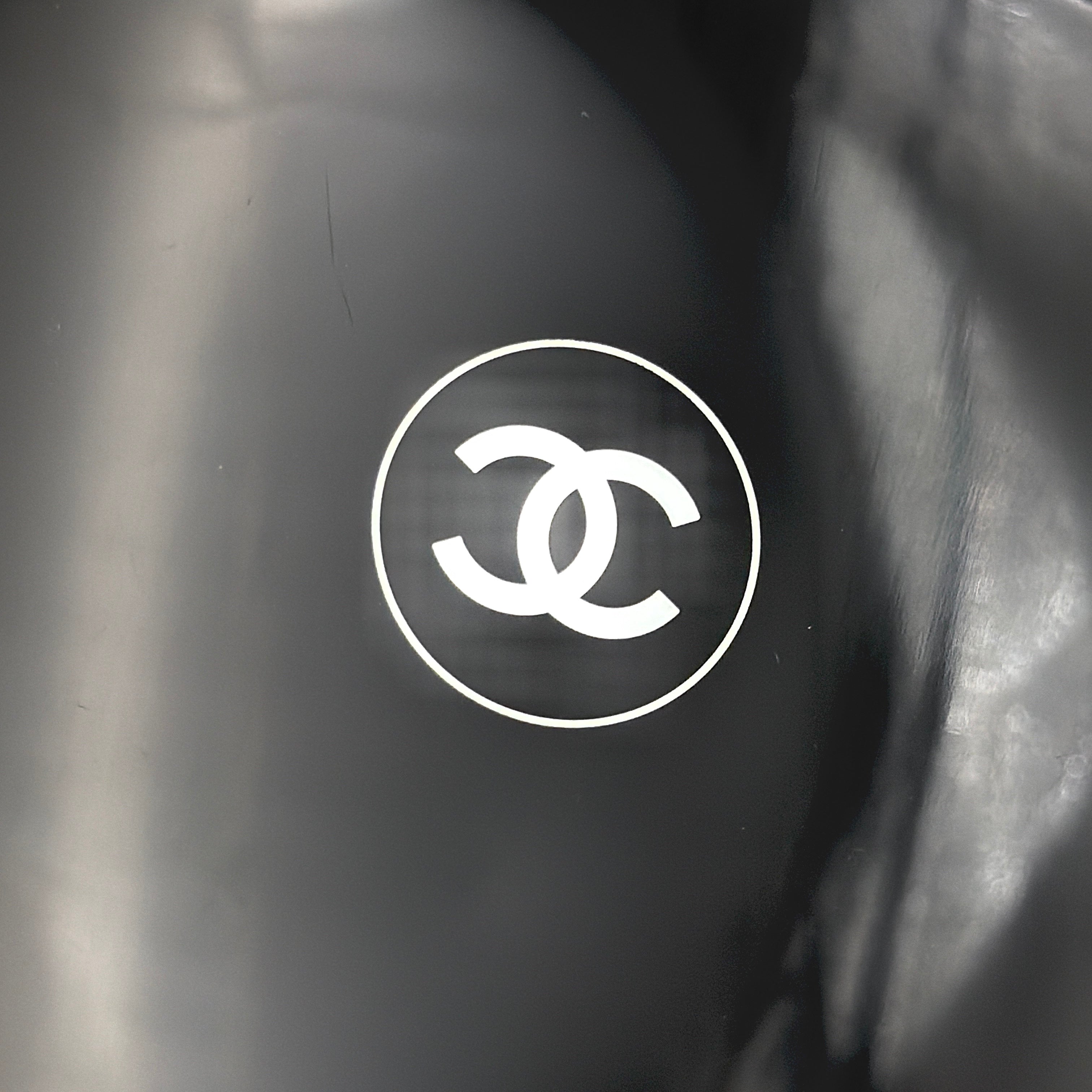 Chanel black hand mirror with white double C logo, presented in its original box with a yellow interior lining.