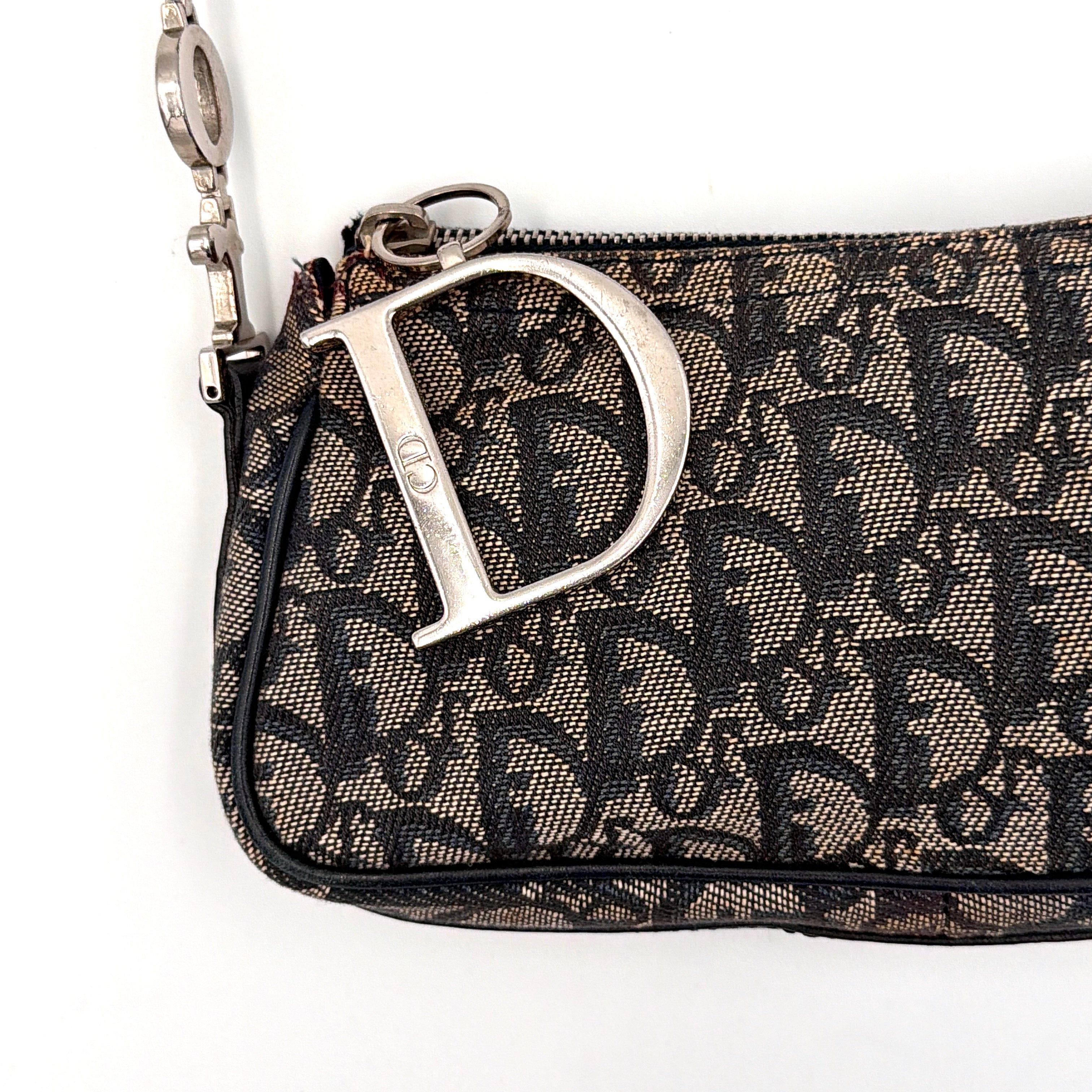 Dior Trotter Charm Pochette bag in grey and navy oblique canvas, featuring bold silver-tone Dior letter charms and a black leather strap.