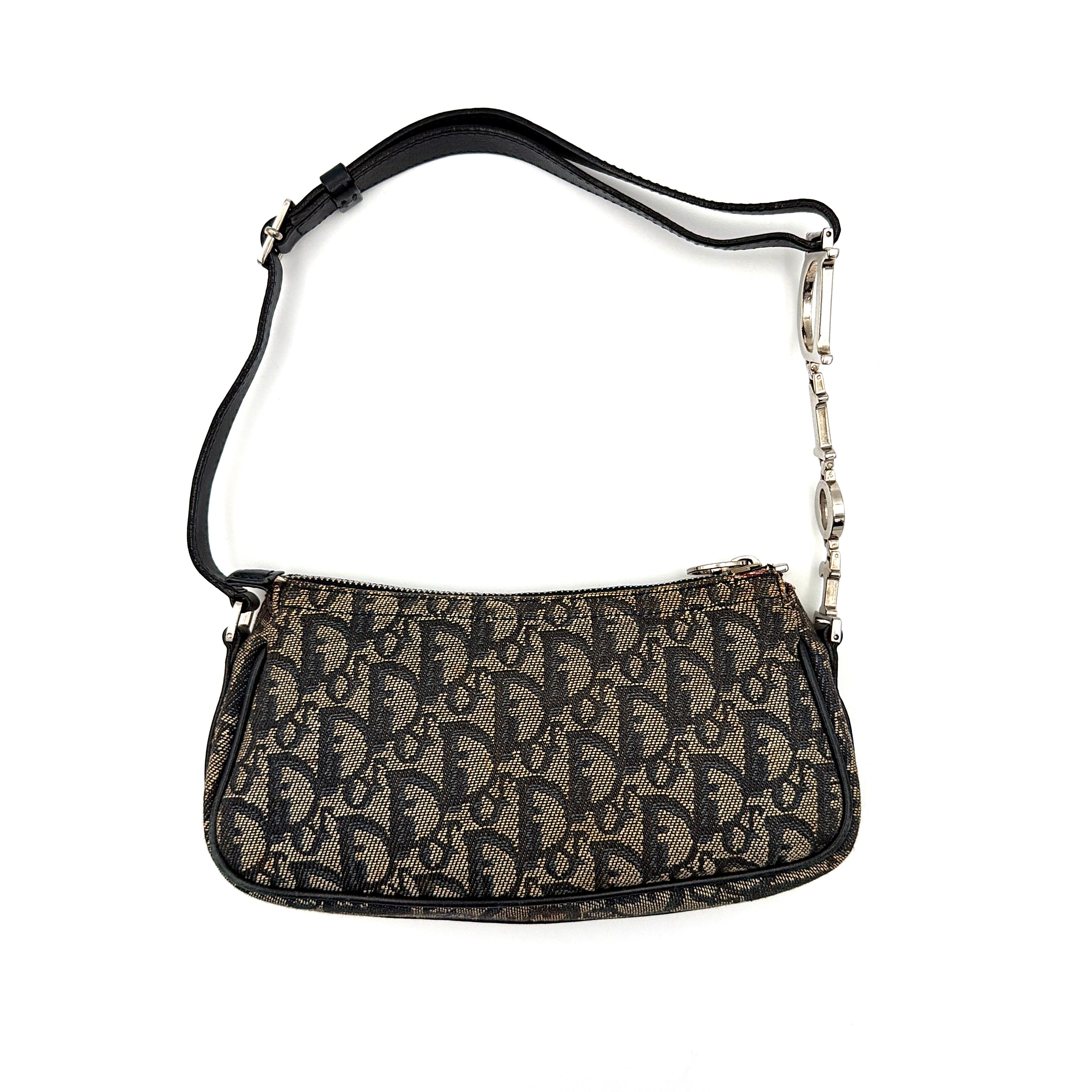 Dior Trotter Charm Pochette bag in grey and navy oblique canvas, featuring bold silver-tone Dior letter charms and a black leather strap.