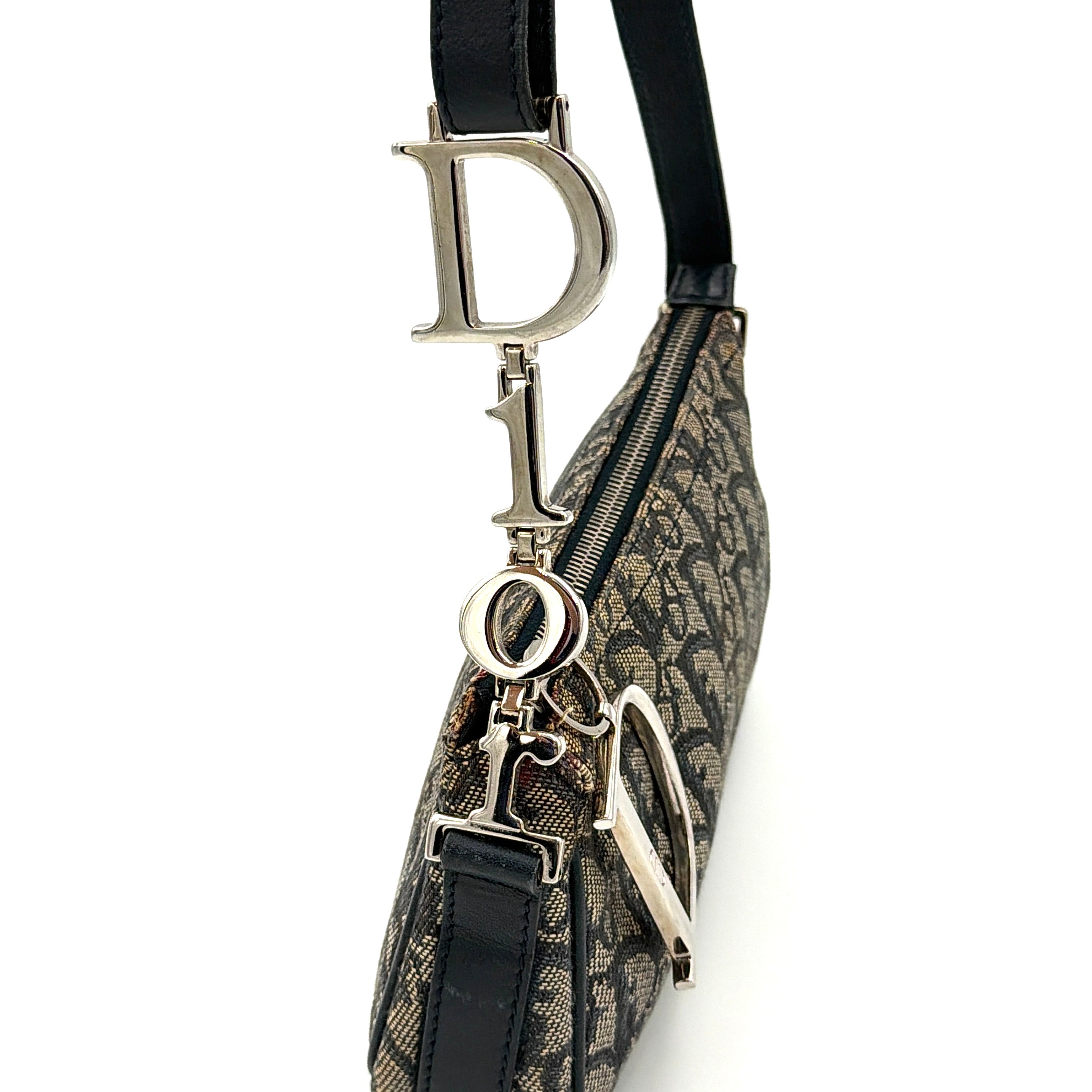 Dior Trotter Charm Pochette bag in grey and navy oblique canvas, featuring bold silver-tone Dior letter charms and a black leather strap.