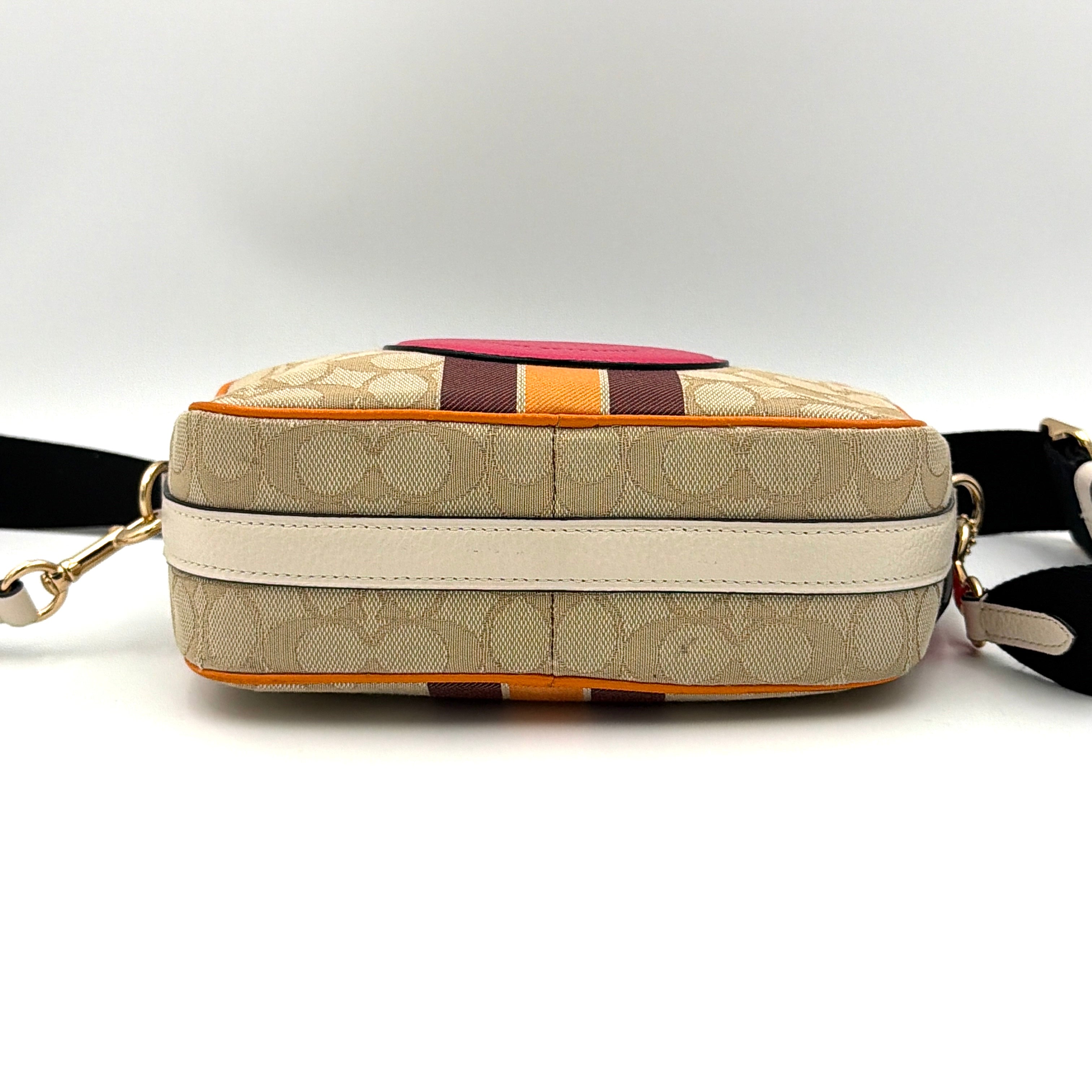 Coach Signature Dempsey Camera Bag in monogram canvas with bold pink logo patch, orange stripes, and wide black strap.