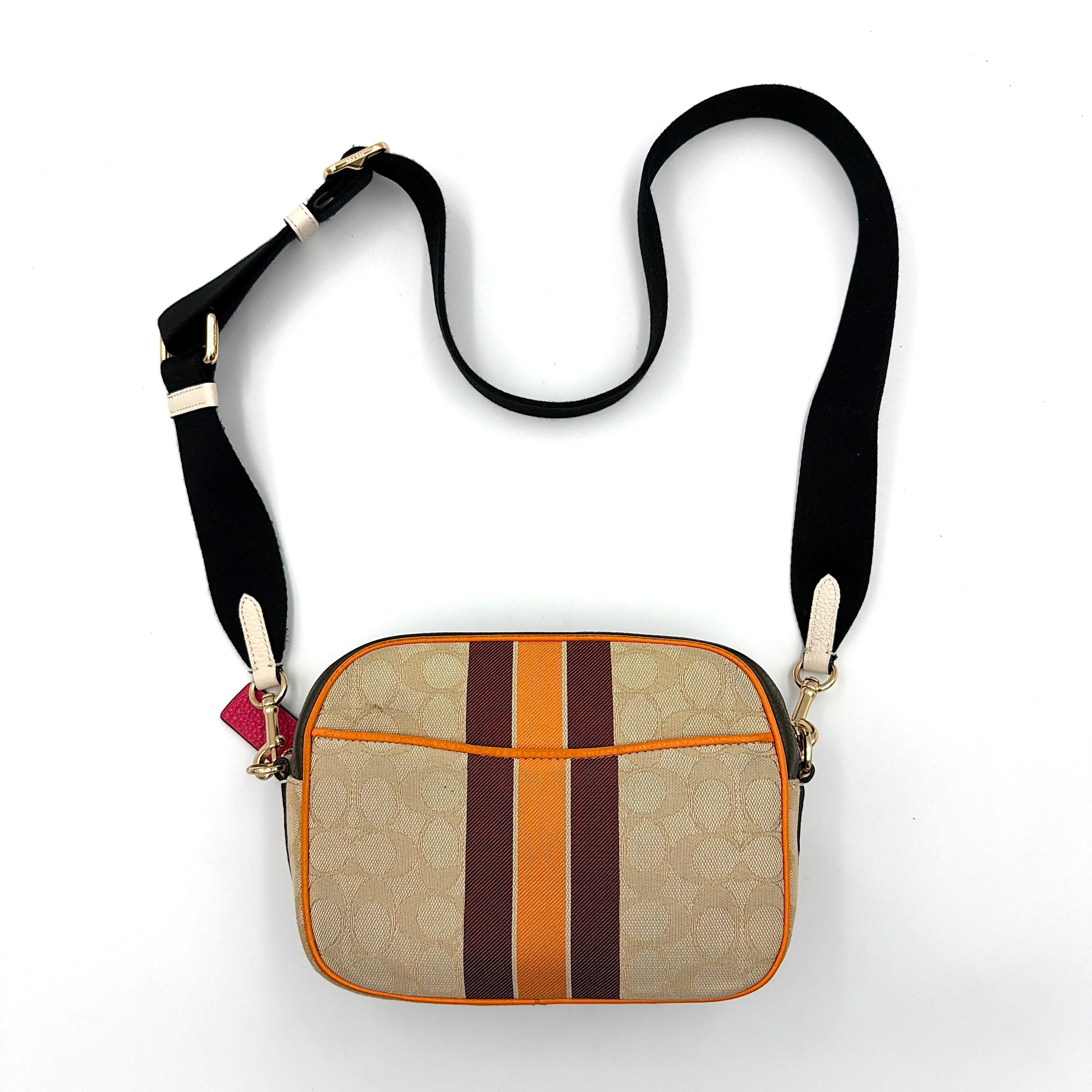 Coach Signature Dempsey Camera Bag in monogram canvas with bold pink logo patch, orange stripes, and wide black strap.