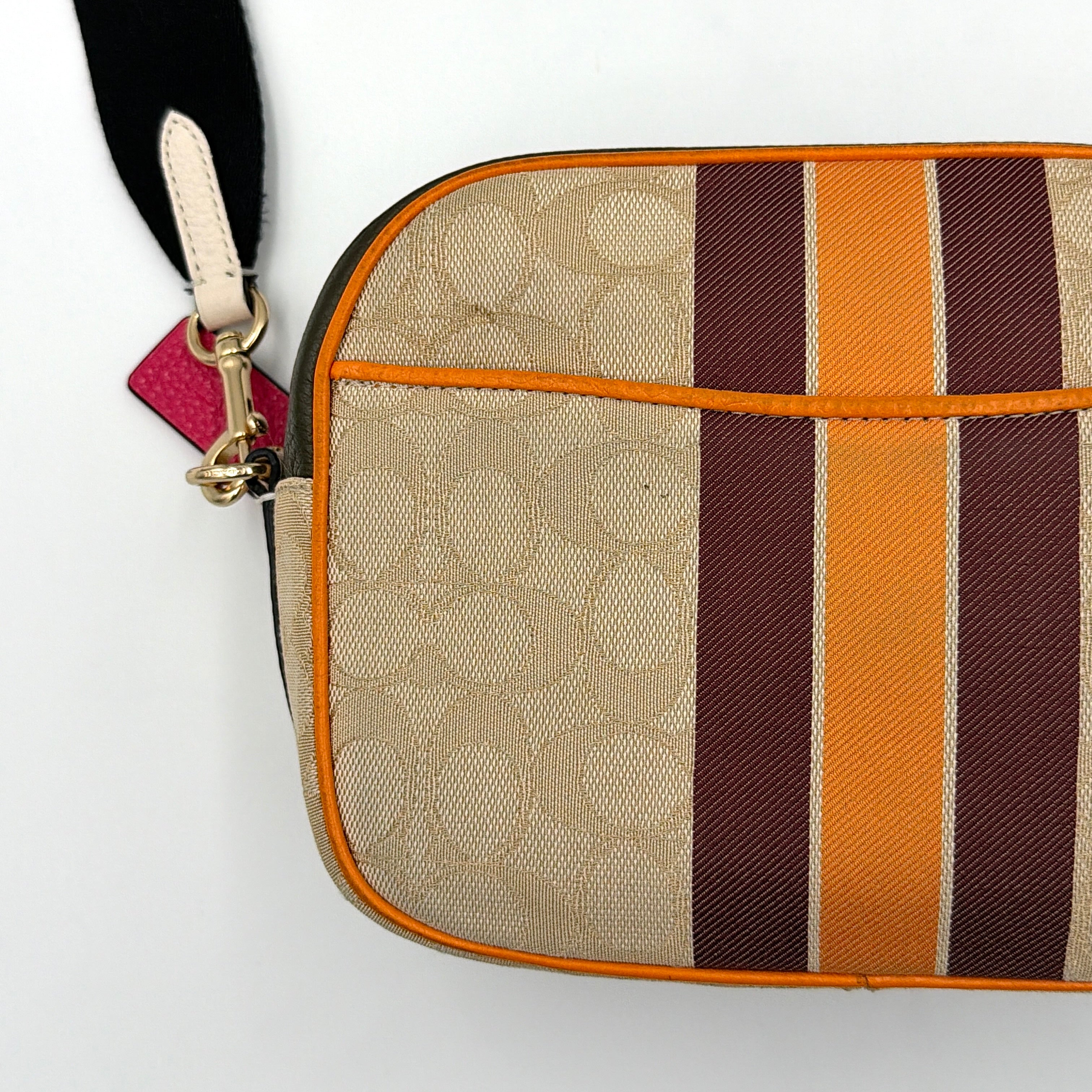 Coach Signature Dempsey Camera Bag in monogram canvas with bold pink logo patch, orange stripes, and wide black strap.