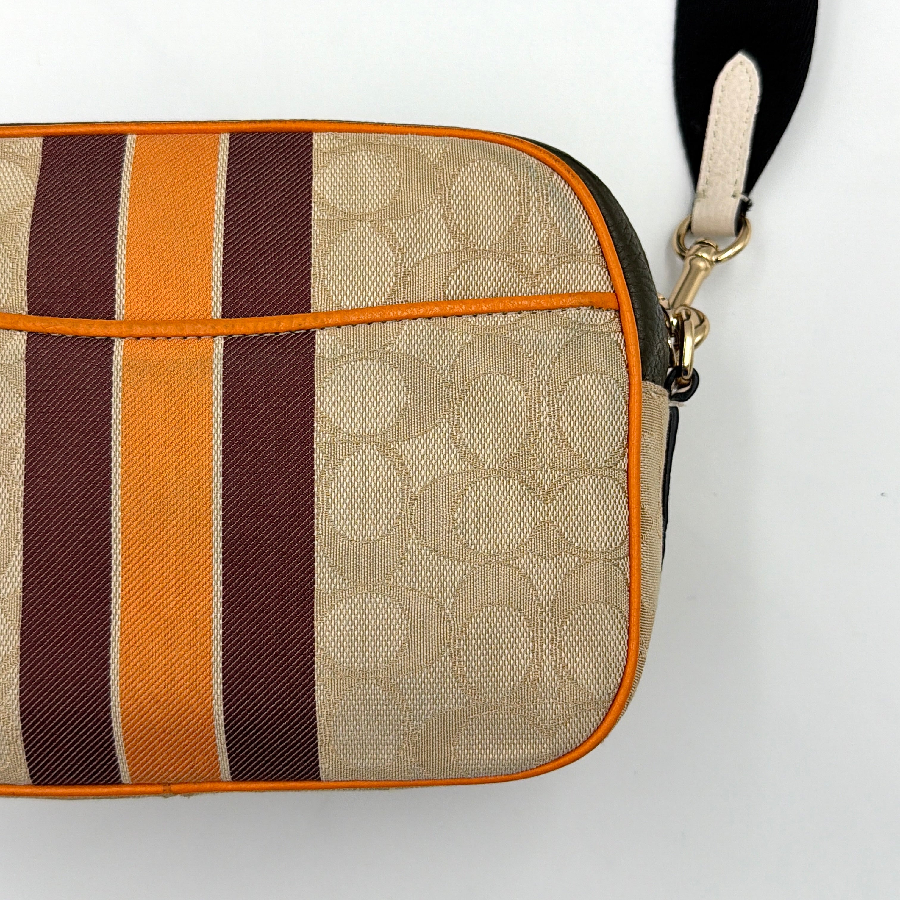 Coach Signature Dempsey Camera Bag in monogram canvas with bold pink logo patch, orange stripes, and wide black strap.