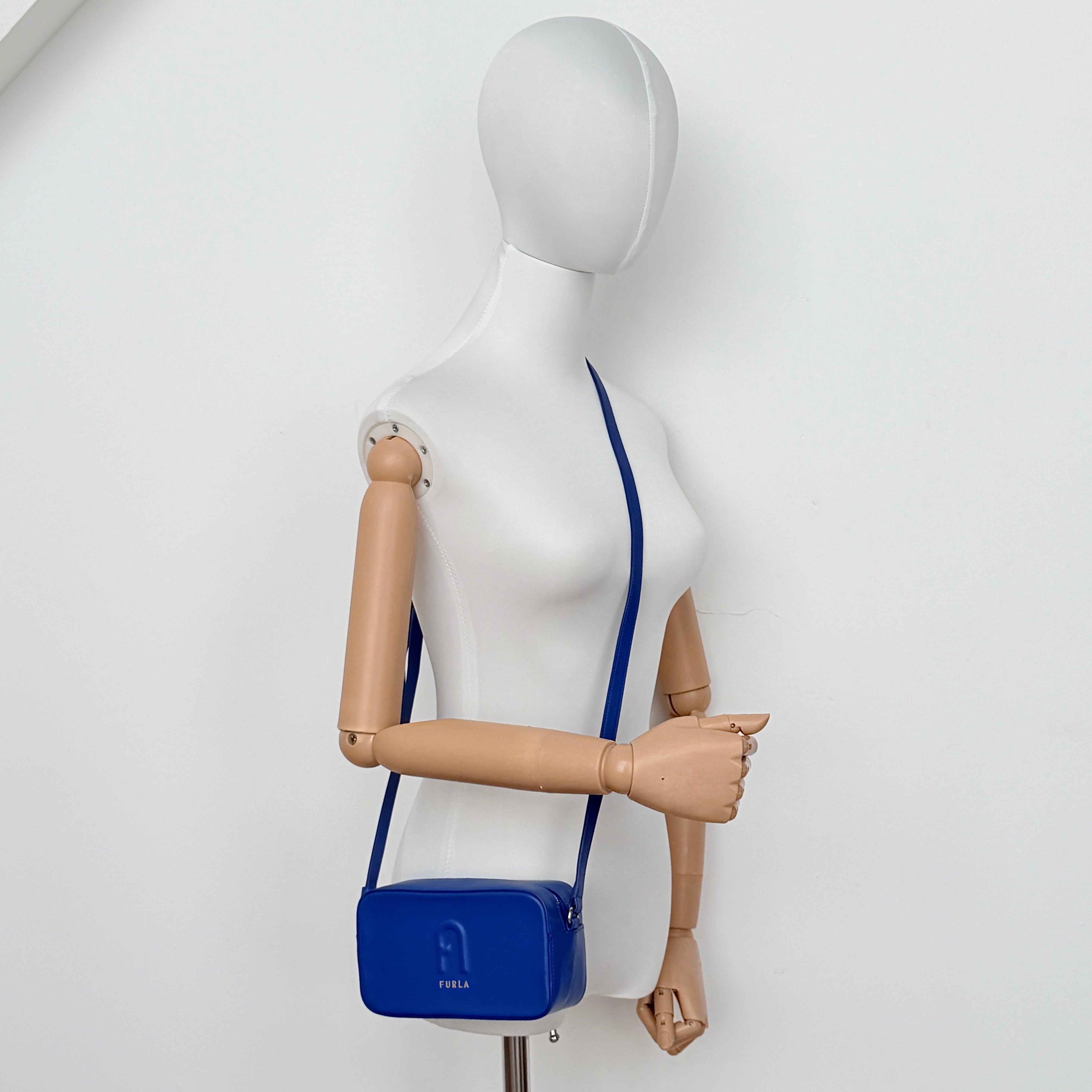 Furla Primula Mini Camera Crossbody Bag in vibrant blue leather with embossed logo, shown with adjustable strap.
