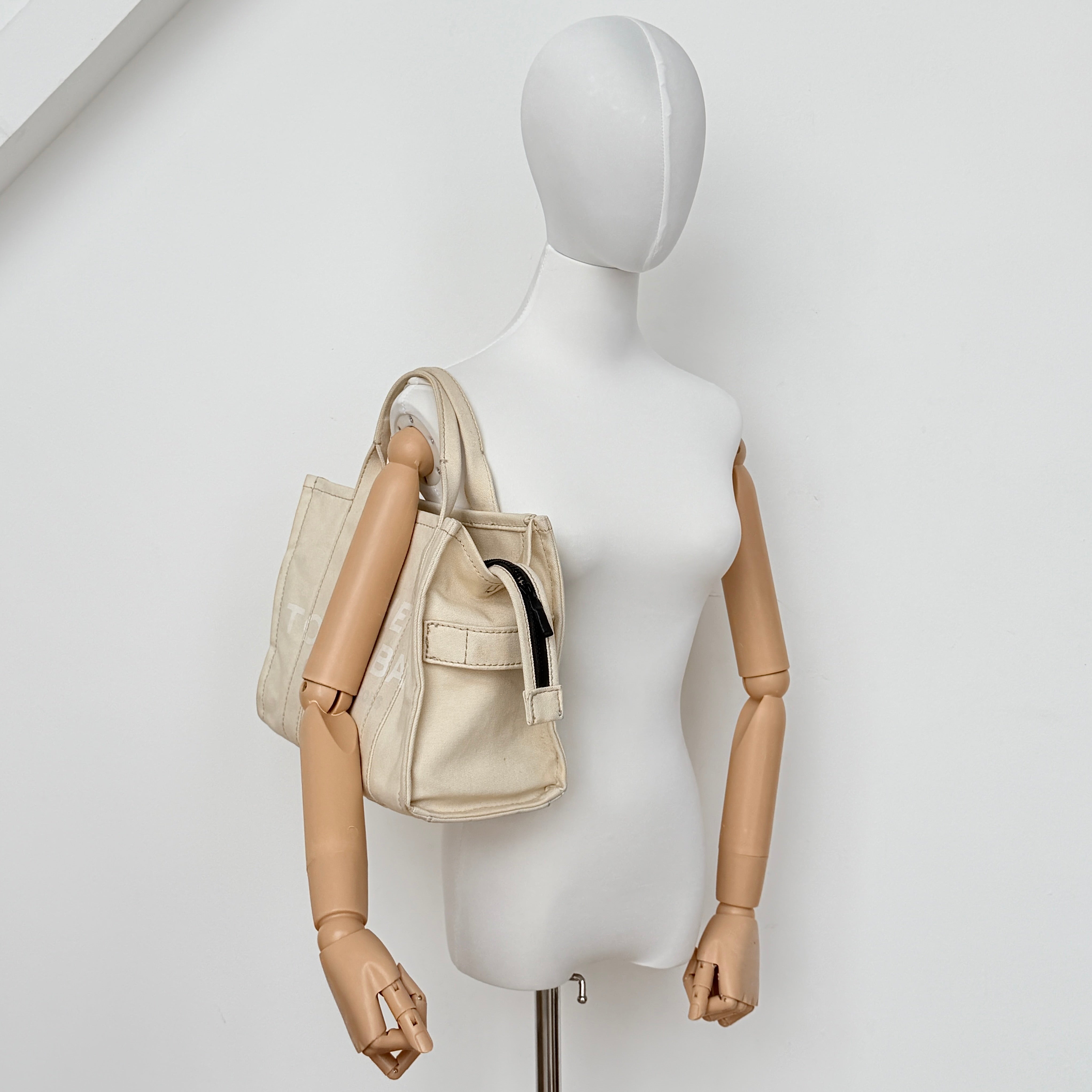 Marc Jacobs The Canvas Tote Bag in beige canvas with bold text, featuring top handles and zip closure.