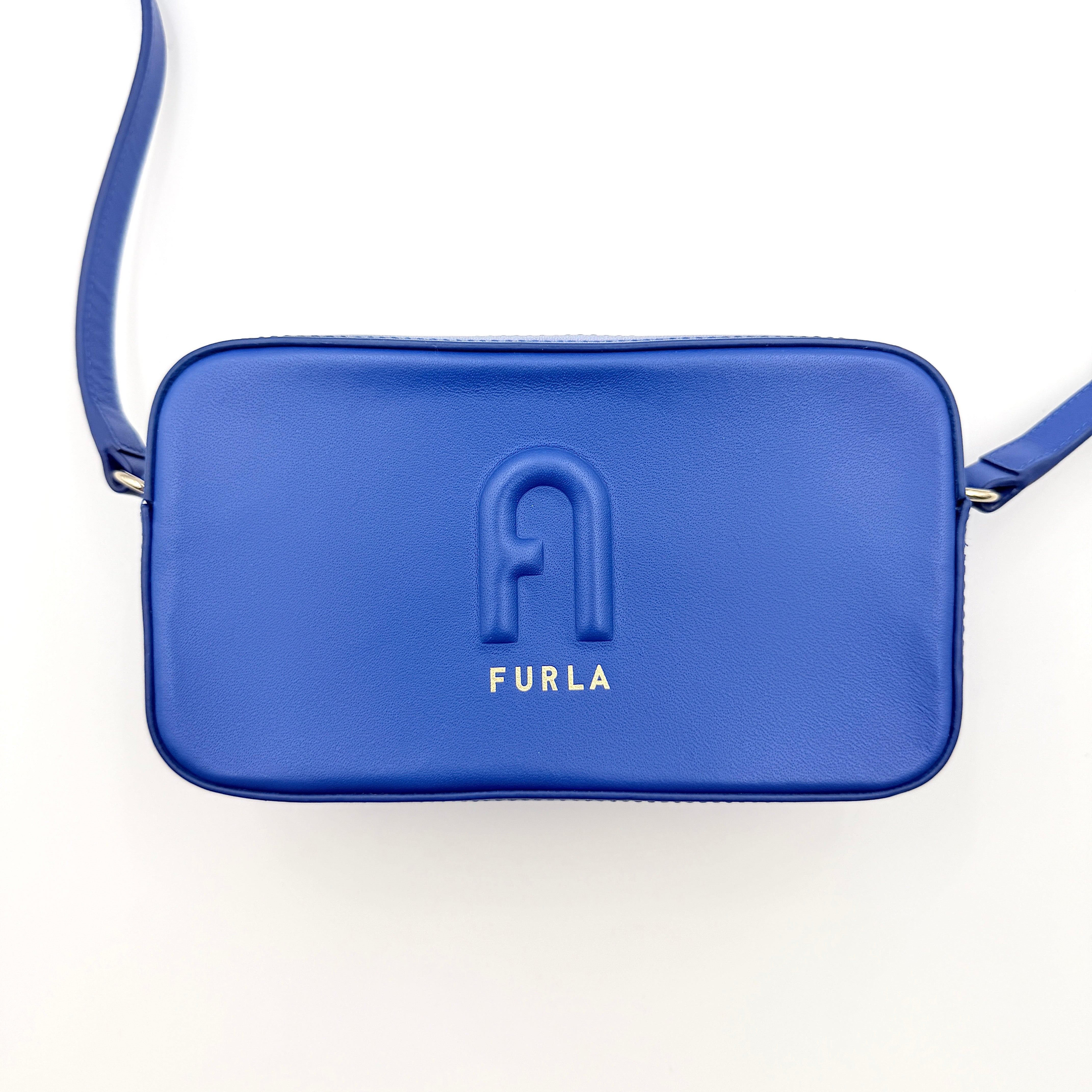 Furla Primula Mini Camera Crossbody Bag in vibrant blue leather with embossed logo, shown with adjustable strap.