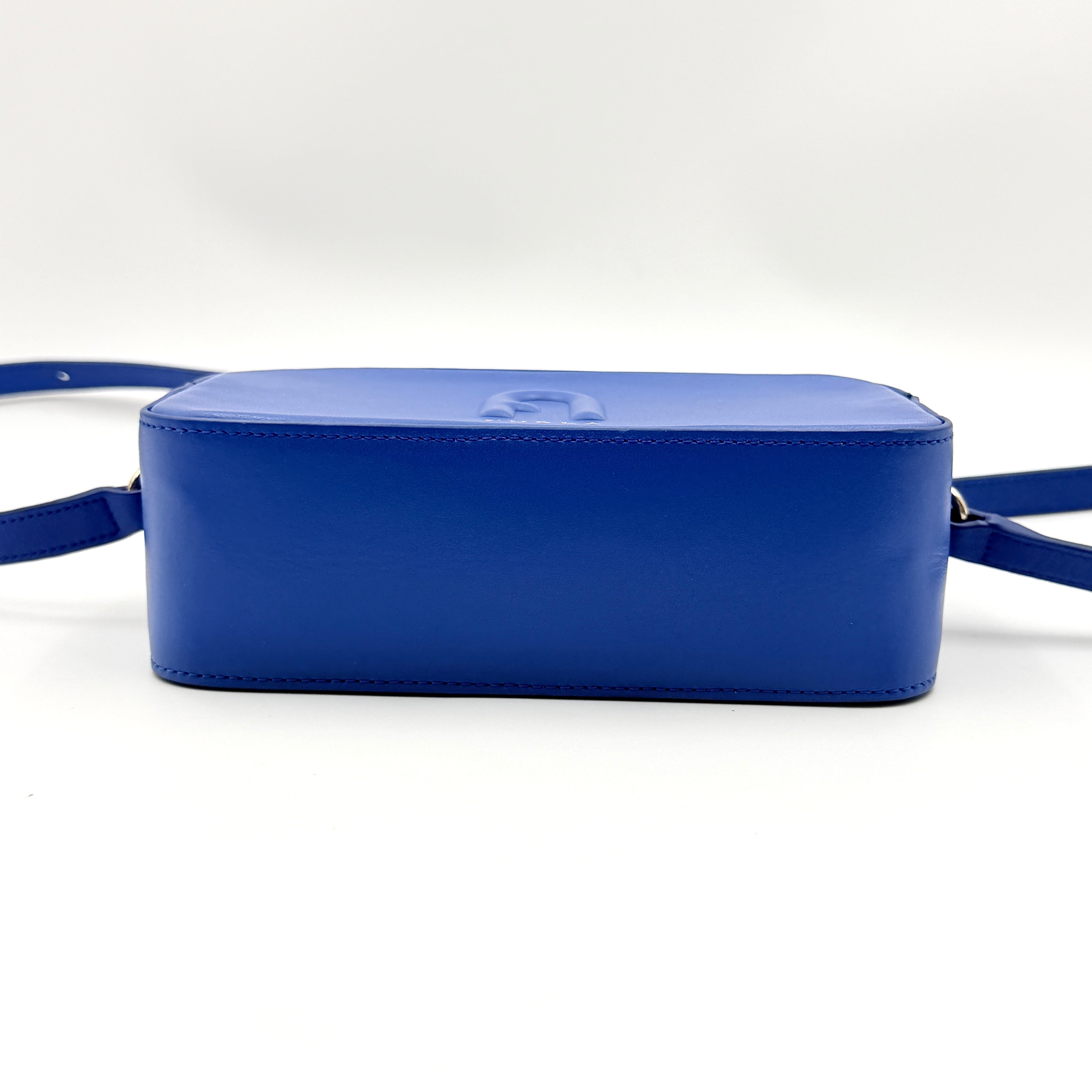 Furla Primula Mini Camera Crossbody Bag in vibrant blue leather with embossed logo, shown with adjustable strap.