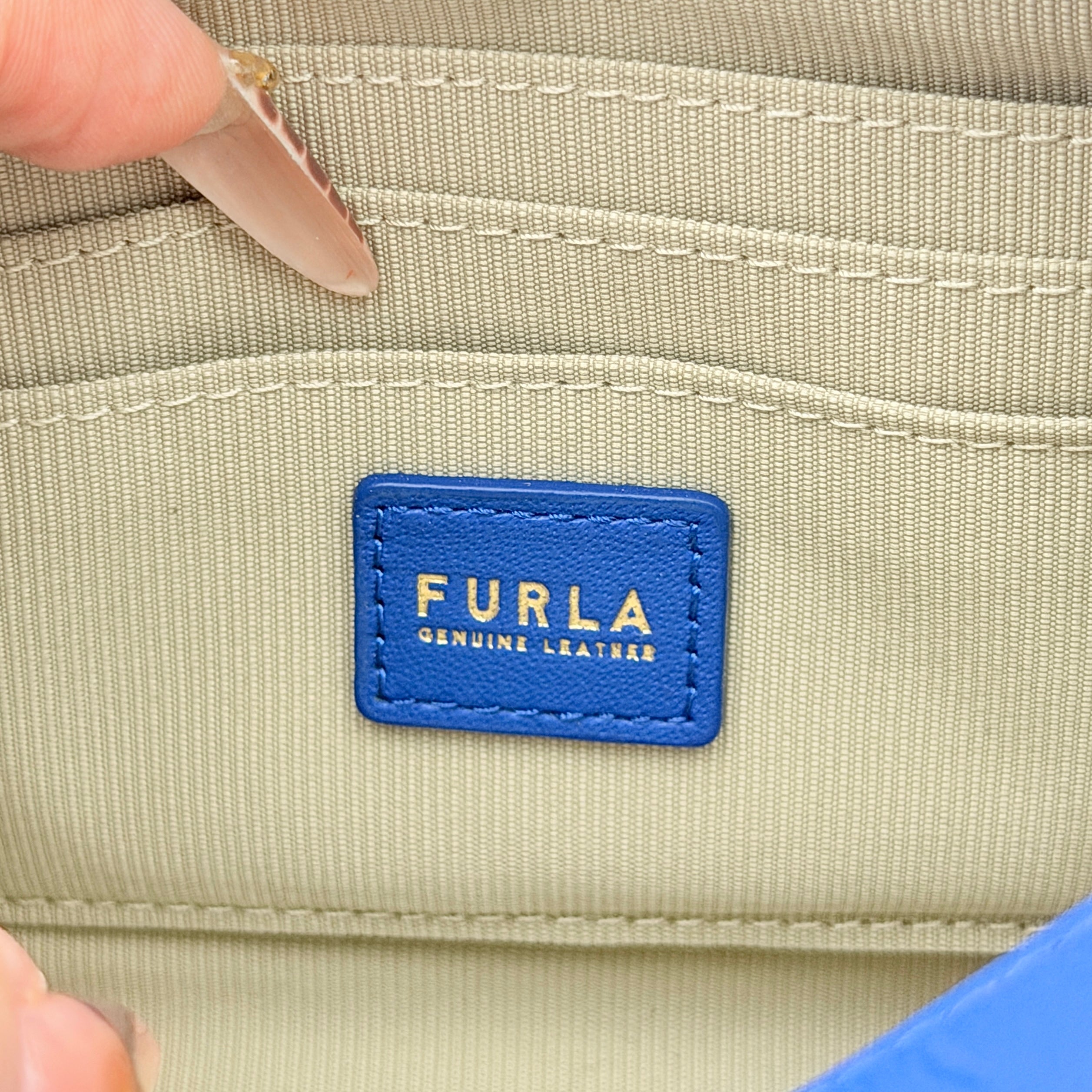 Furla Primula Mini Camera Crossbody Bag in vibrant blue leather with embossed logo, shown with adjustable strap.