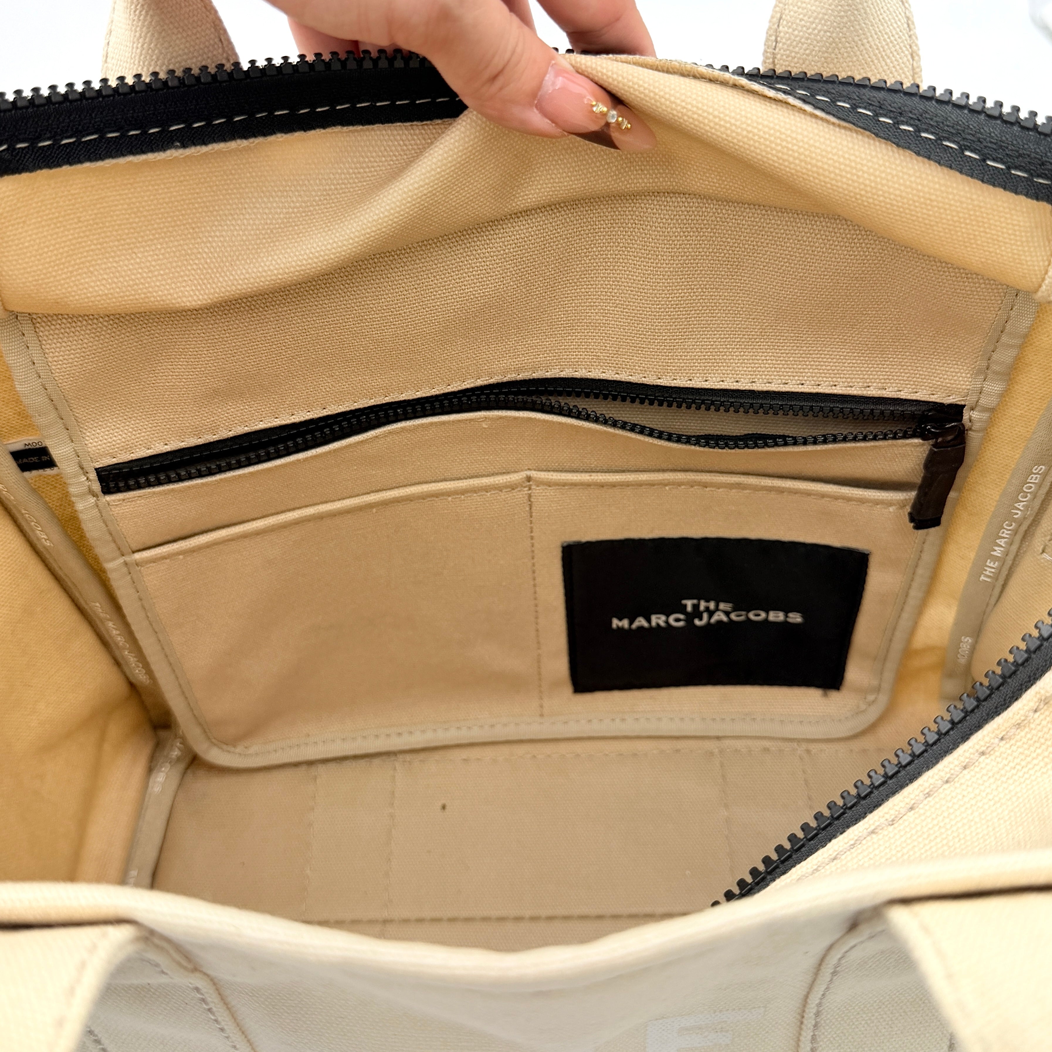 Marc Jacobs The Canvas Tote Bag in beige canvas with bold text, featuring top handles and zip closure.