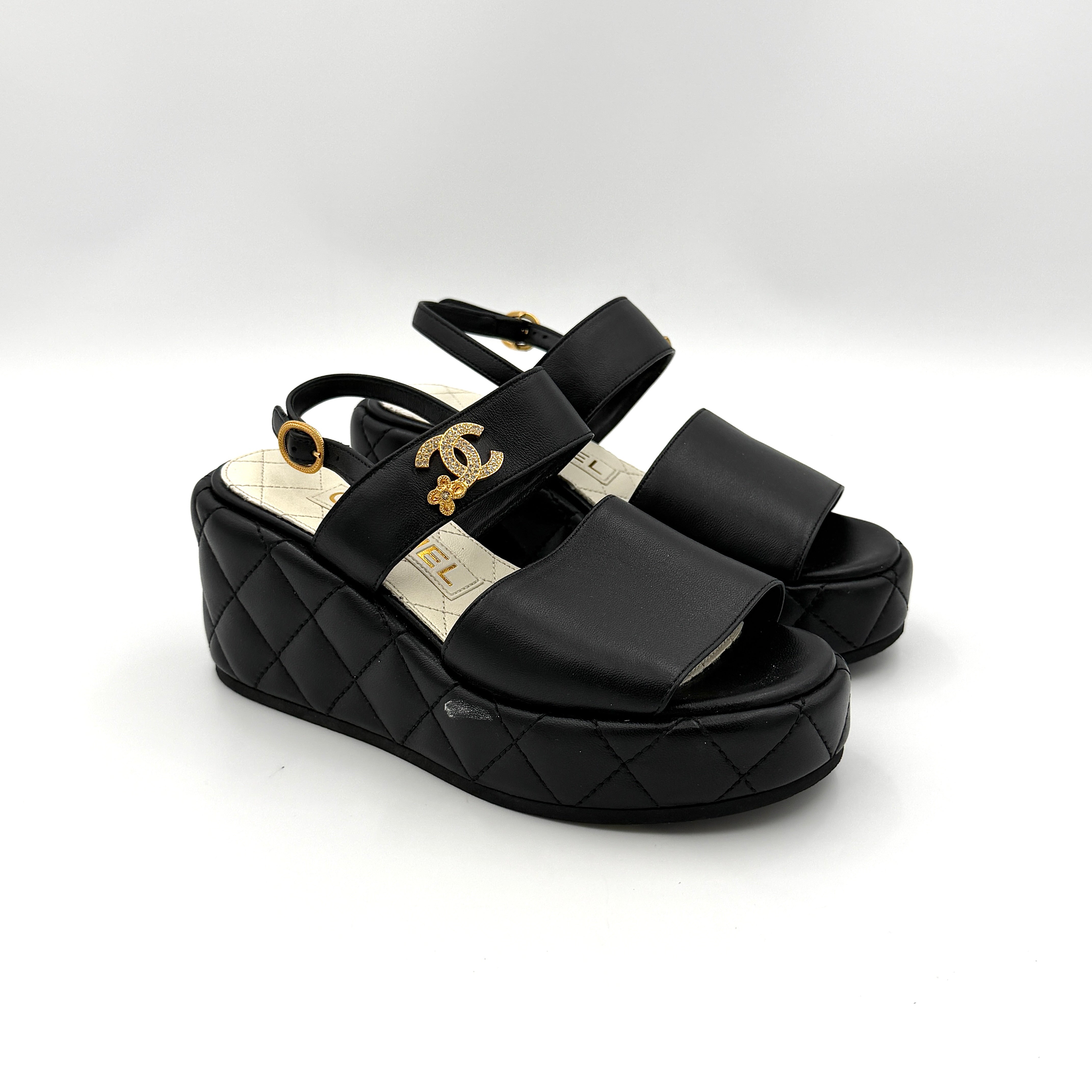 Chanel black quilted leather wedge platform sandals with gold crystal CC hardware and ankle strap detailing.