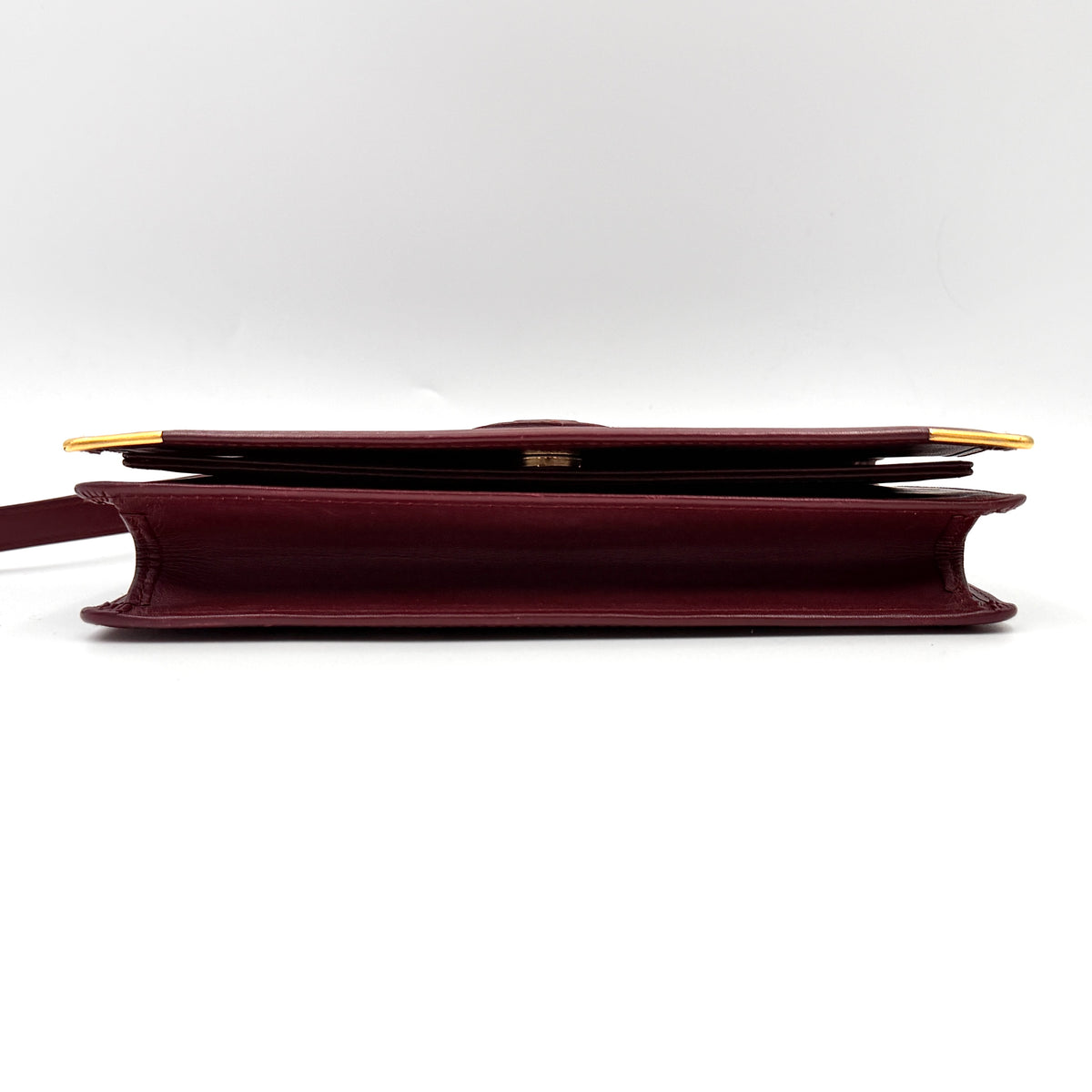Cartier Must de Cartier wristlet clutch in burgundy leather with gold-tone corners and wrist strap, pictured with authenticity card and booklet.