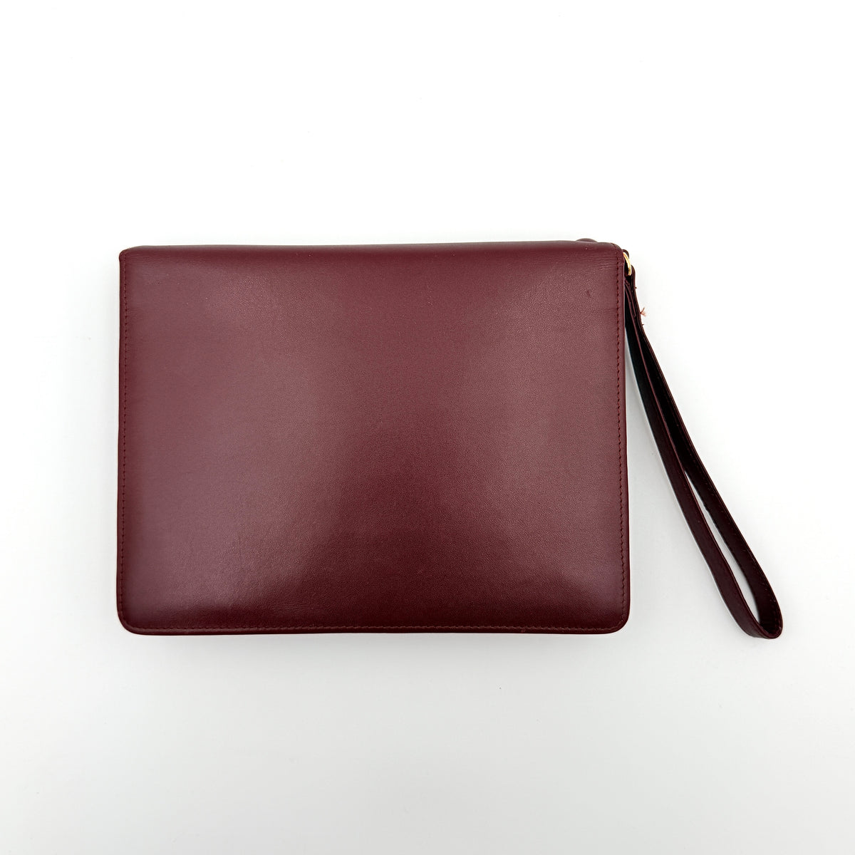 Cartier Must de Cartier wristlet clutch in burgundy leather with gold-tone corners and wrist strap, pictured with authenticity card and booklet.