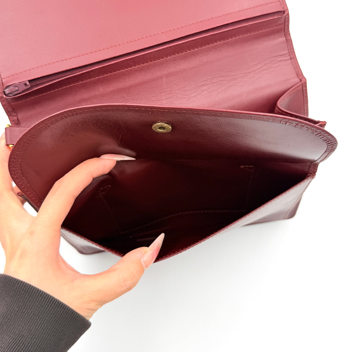 Cartier Must de Cartier wristlet clutch in burgundy leather with gold-tone corners and wrist strap, pictured with authenticity card and booklet.