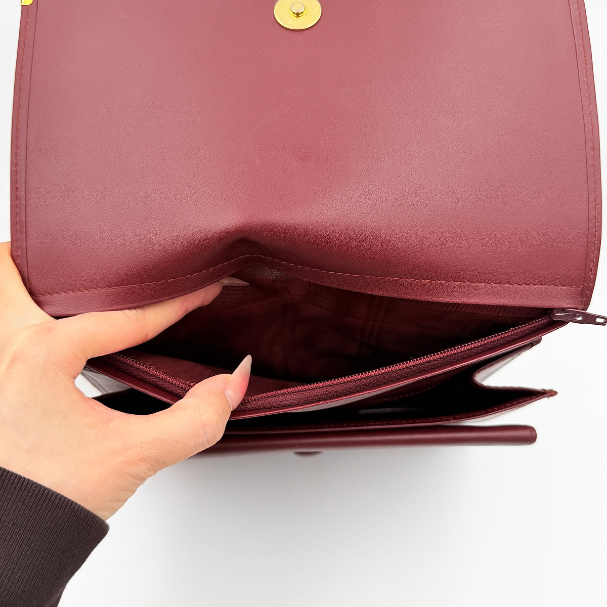 Cartier Must de Cartier wristlet clutch in burgundy leather with gold-tone corners and wrist strap, pictured with authenticity card and booklet.