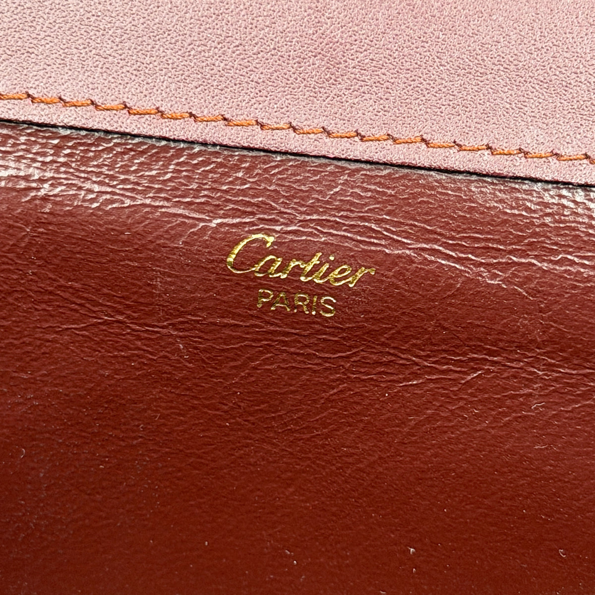 Cartier Must de Cartier wristlet clutch in burgundy leather with gold-tone corners and wrist strap, pictured with authenticity card and booklet.