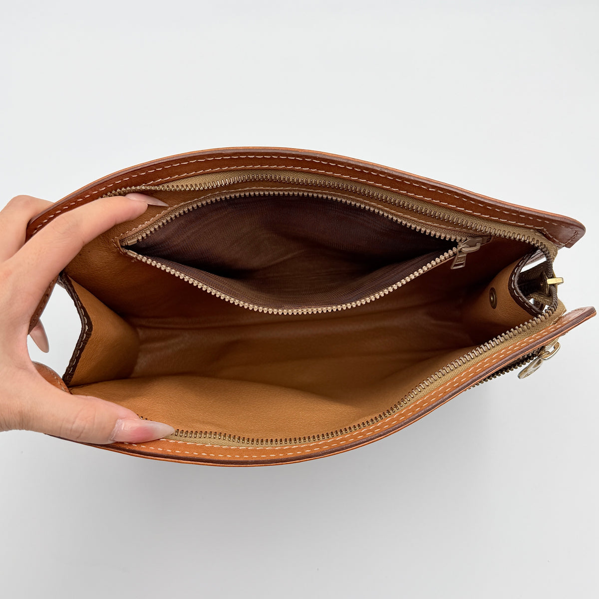 Celine Triomphe Macadam Clutch Bag in brown coated canvas with tan leather trim and gold zip, displayed against a white background.