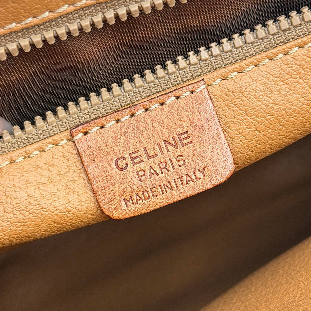 Celine Triomphe Macadam Clutch Bag in brown coated canvas with tan leather trim and gold zip, displayed against a white background.
