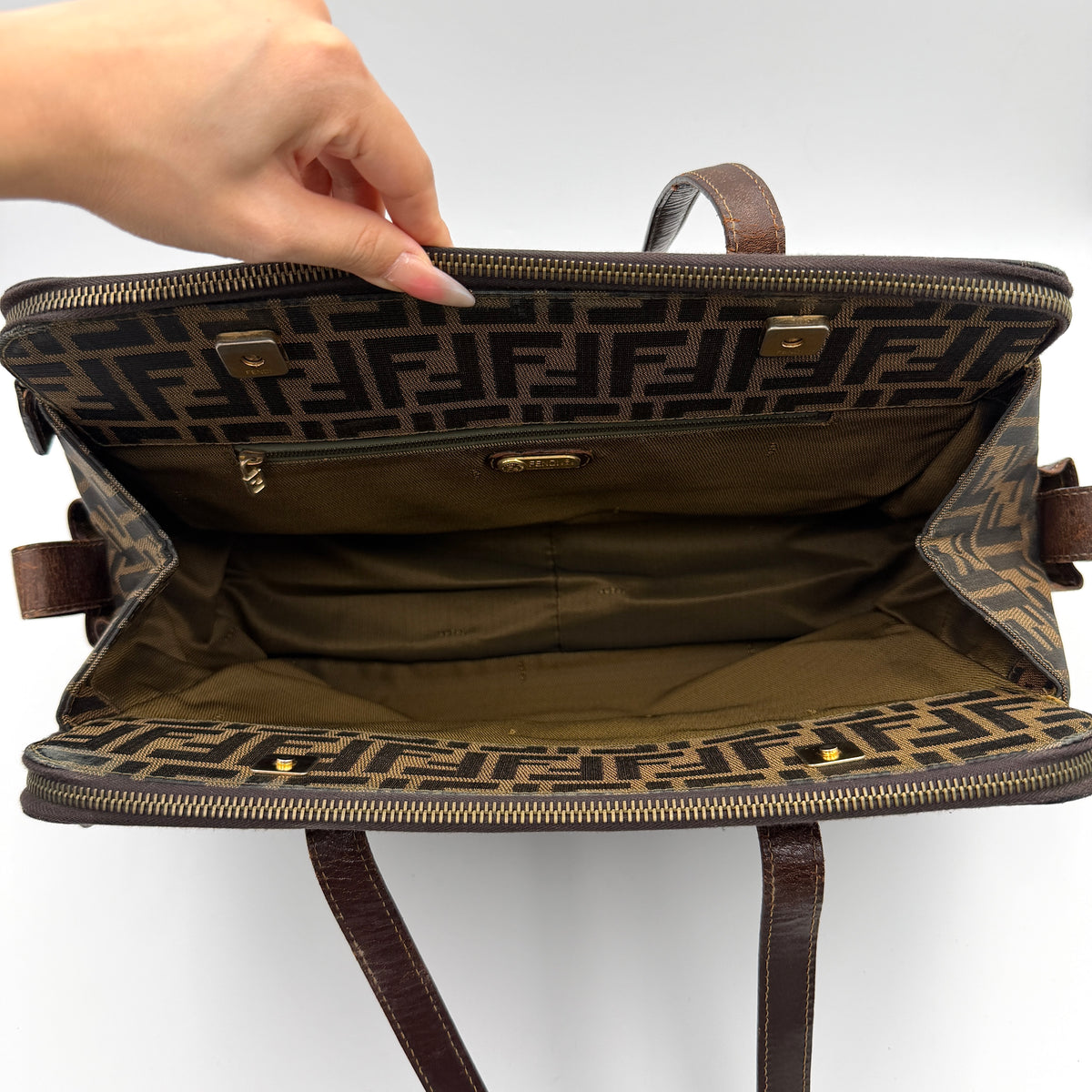 Fendi FF Zucca Double Zip Tote Bag in brown monogram canvas with leather straps and side pocket detail, shown on a yellow dust bag.