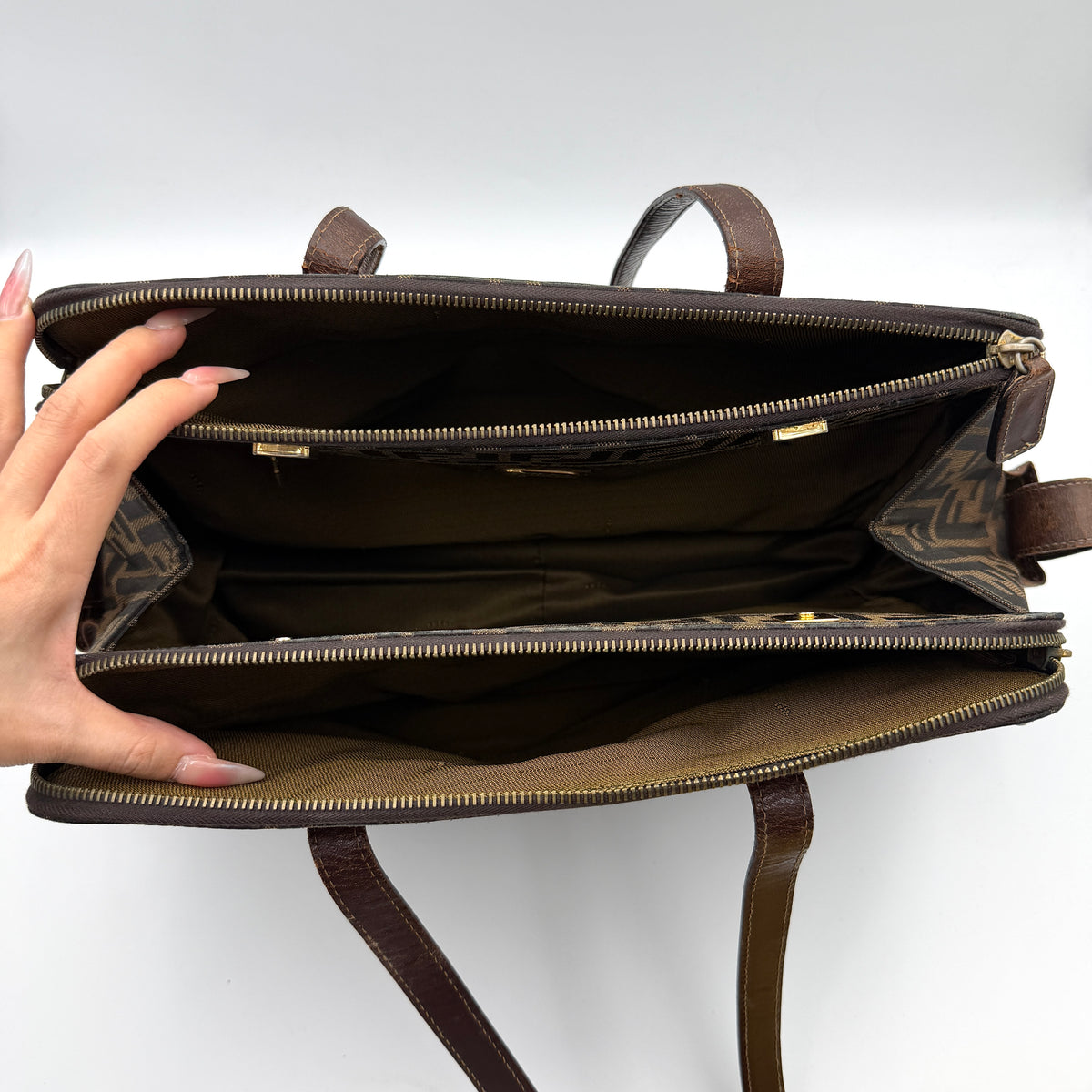 Fendi FF Zucca Double Zip Tote Bag in brown monogram canvas with leather straps and side pocket detail, shown on a yellow dust bag.