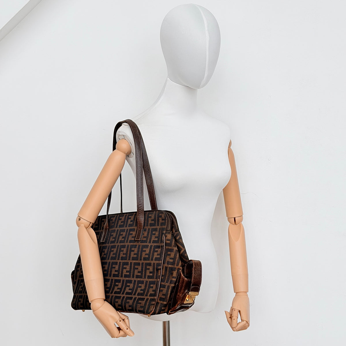 Fendi FF Zucca Double Zip Tote Bag in brown monogram canvas with leather straps and side pocket detail, shown on a yellow dust bag.