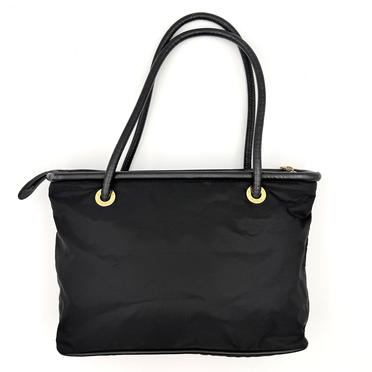 Black Celine nylon tote bag with gold circle logo hardware and leather handles, photographed flat on a white background.