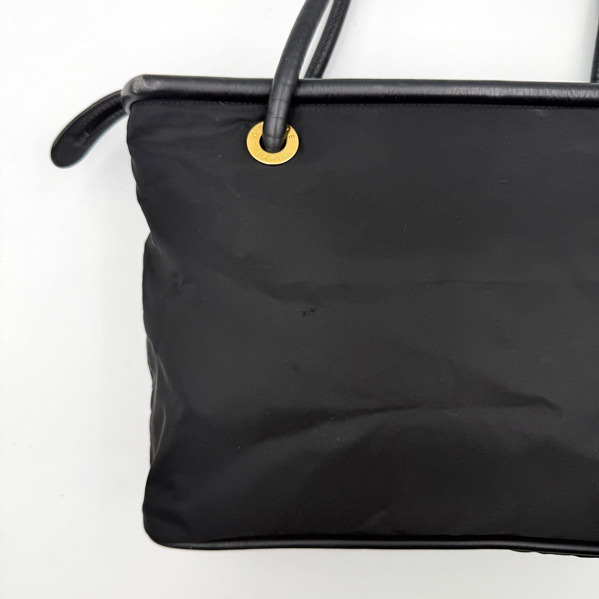 Black Celine nylon tote bag with gold circle logo hardware and leather handles, photographed flat on a white background.