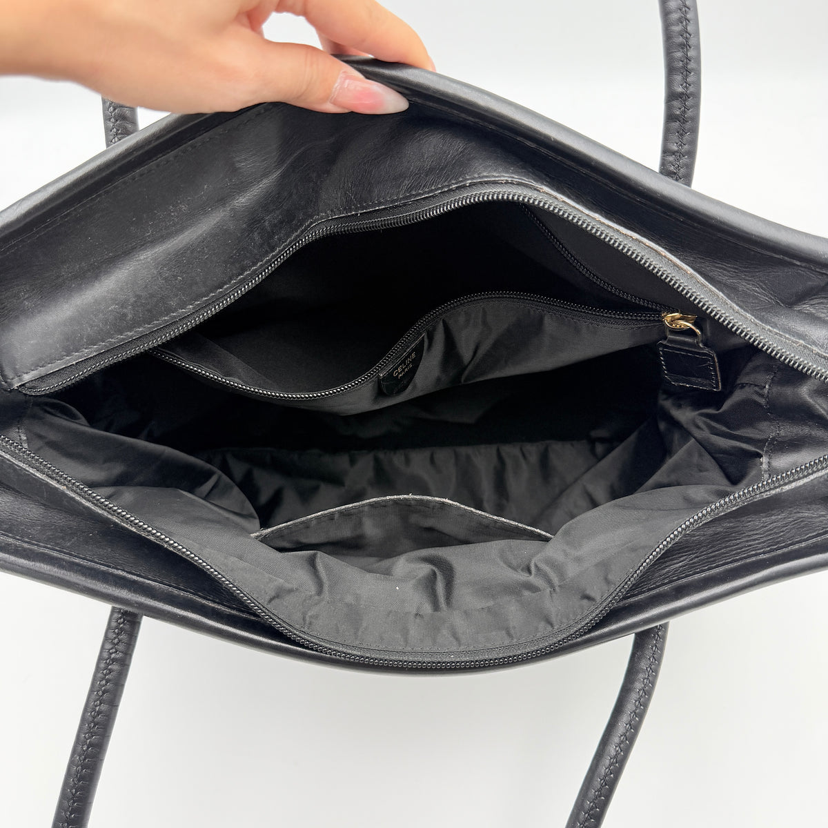 Black Celine nylon tote bag with gold circle logo hardware and leather handles, photographed flat on a white background.