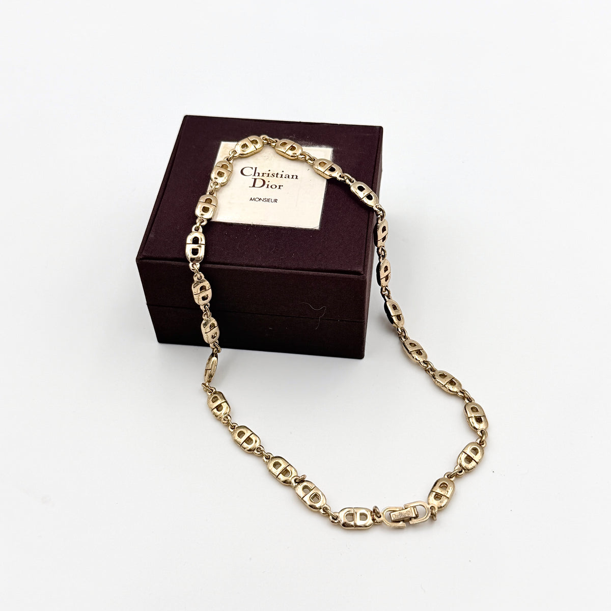 Christian Dior gold CD logo link choker necklace displayed on its original box.