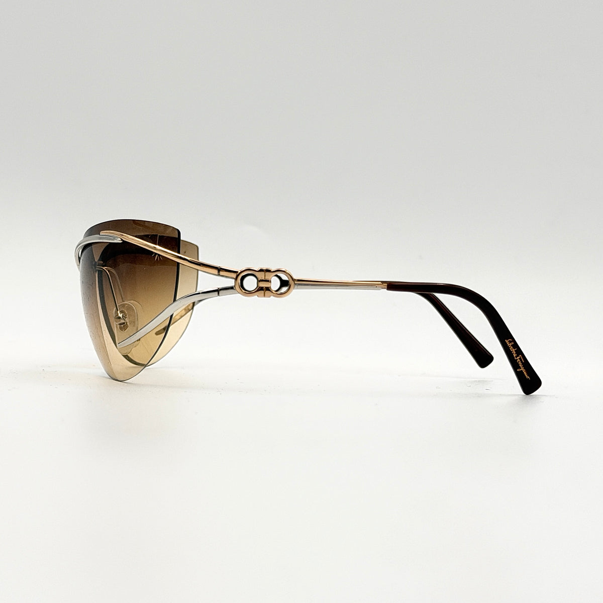 Salvatore Ferragamo rimless sunglasses with gradient brown lenses and sculptural Gancini metal arms on a white background.