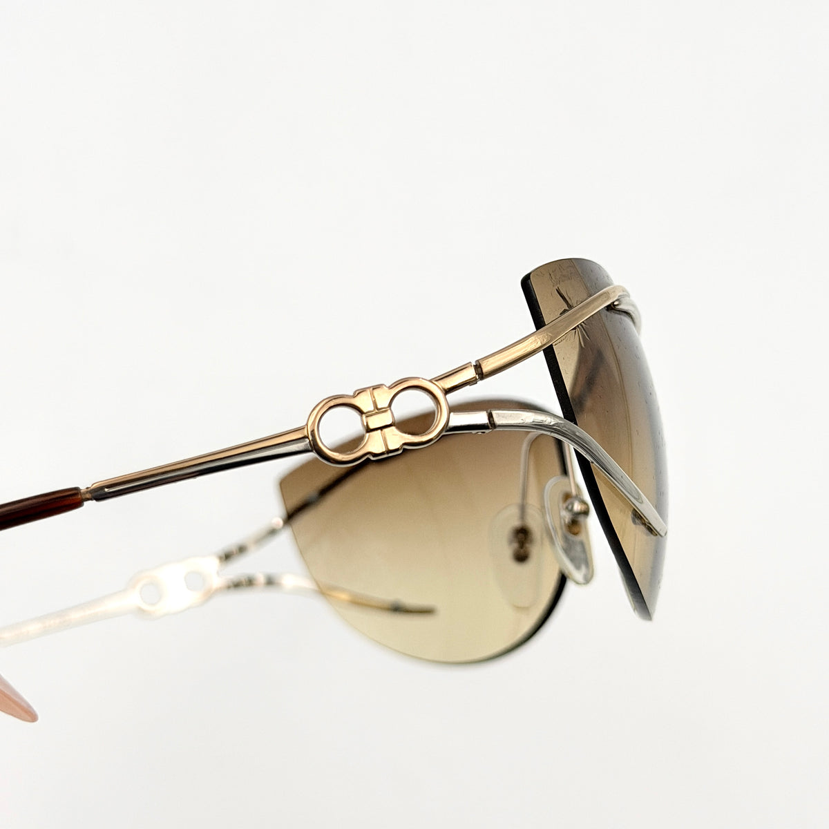 Salvatore Ferragamo rimless sunglasses with gradient brown lenses and sculptural Gancini metal arms on a white background.
