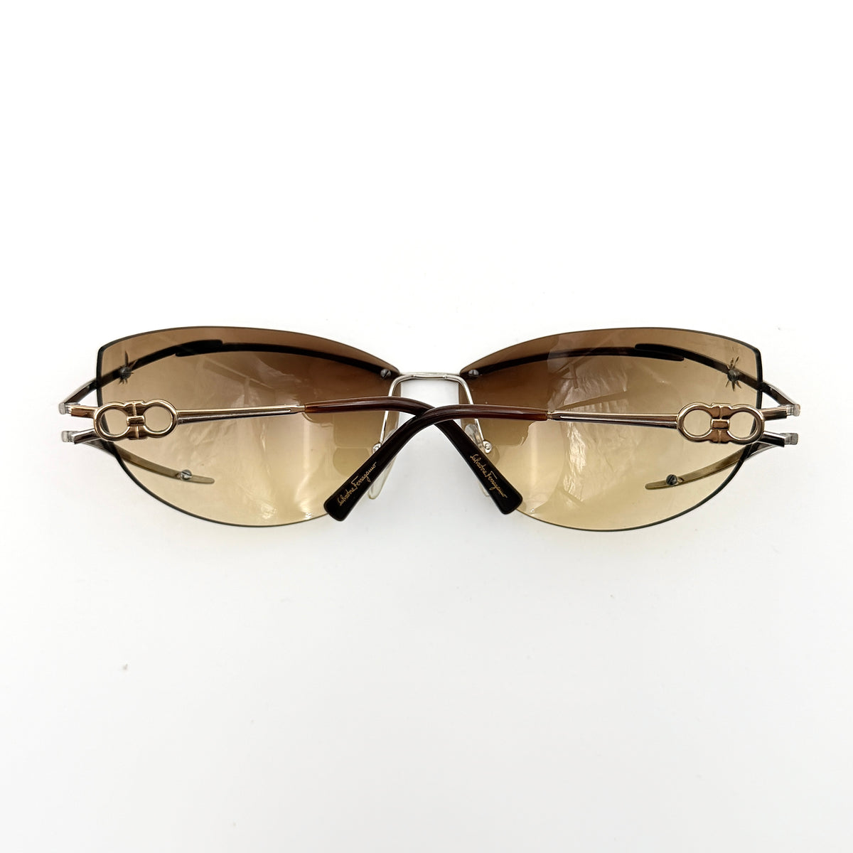 Salvatore Ferragamo rimless sunglasses with gradient brown lenses and sculptural Gancini metal arms on a white background.