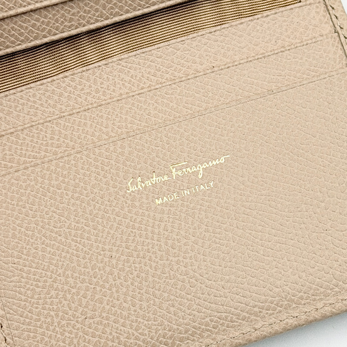 Salvatore Ferragamo beige grained leather compact bifold wallet with gold Gancini hardware, photographed on a white background.