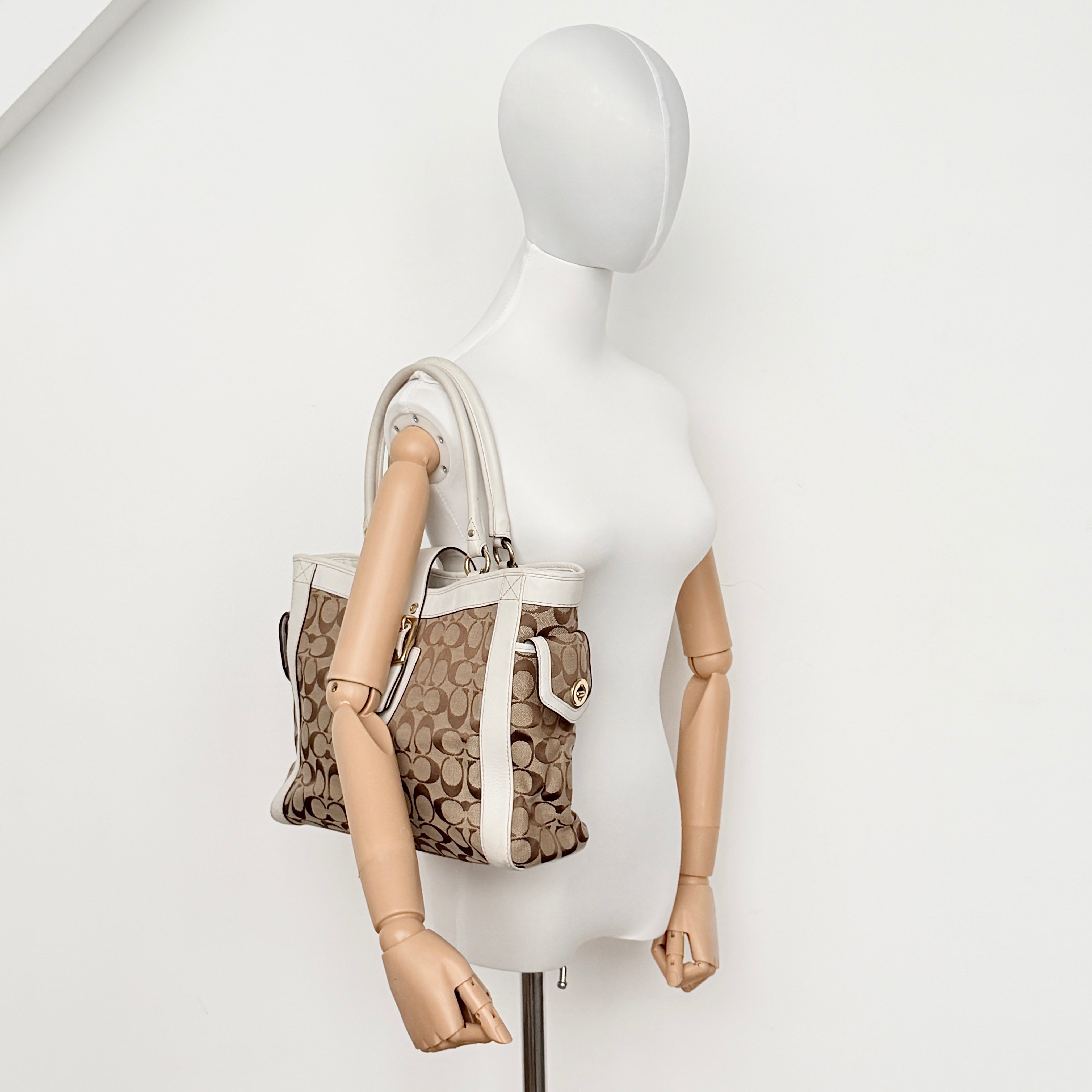 Coach Signature Soho Buckle Tote in beige canvas with white leather trim and gold-tone hardware, displayed against a clean background.