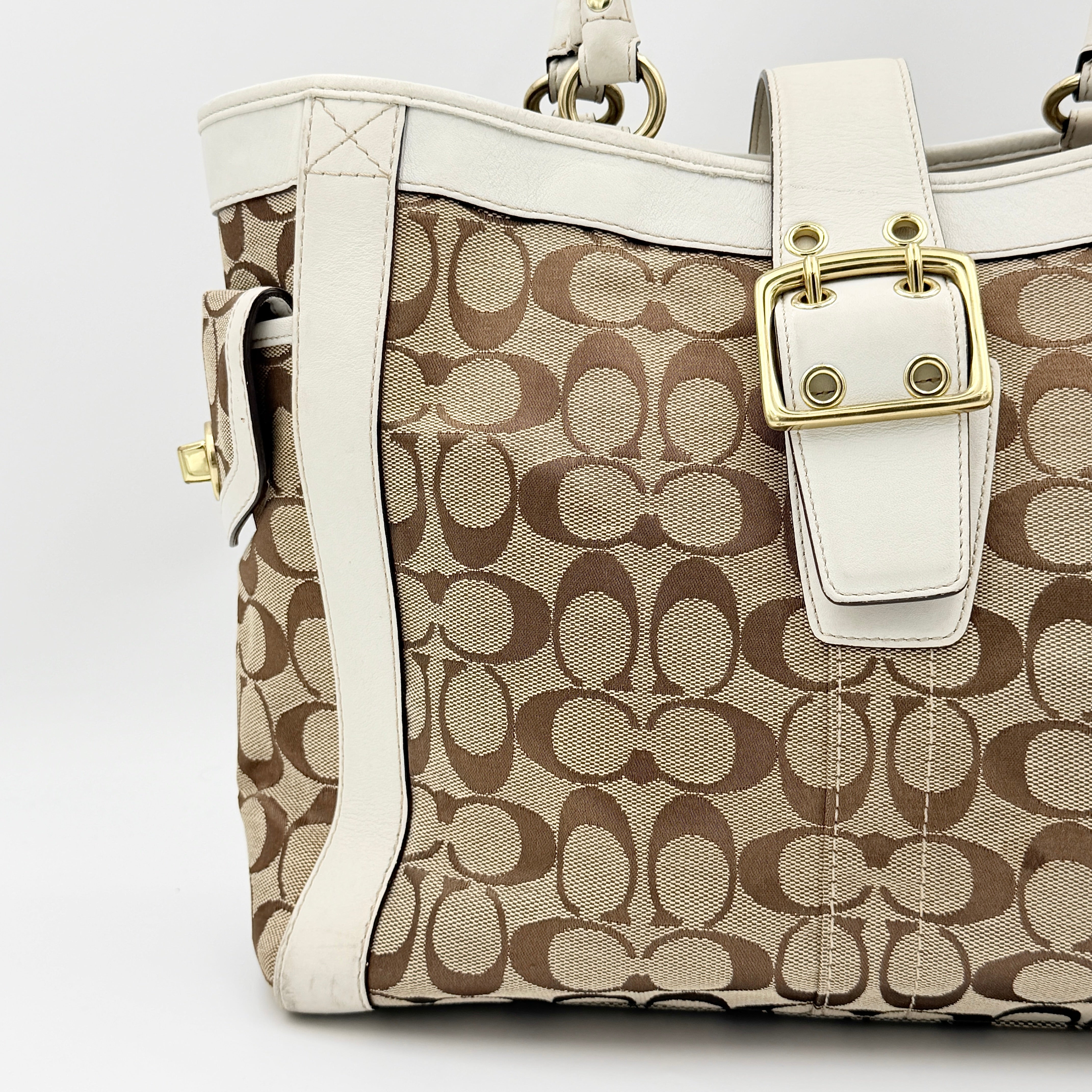 Coach Signature Soho Buckle Tote in beige canvas with white leather trim and gold-tone hardware, displayed against a clean background.